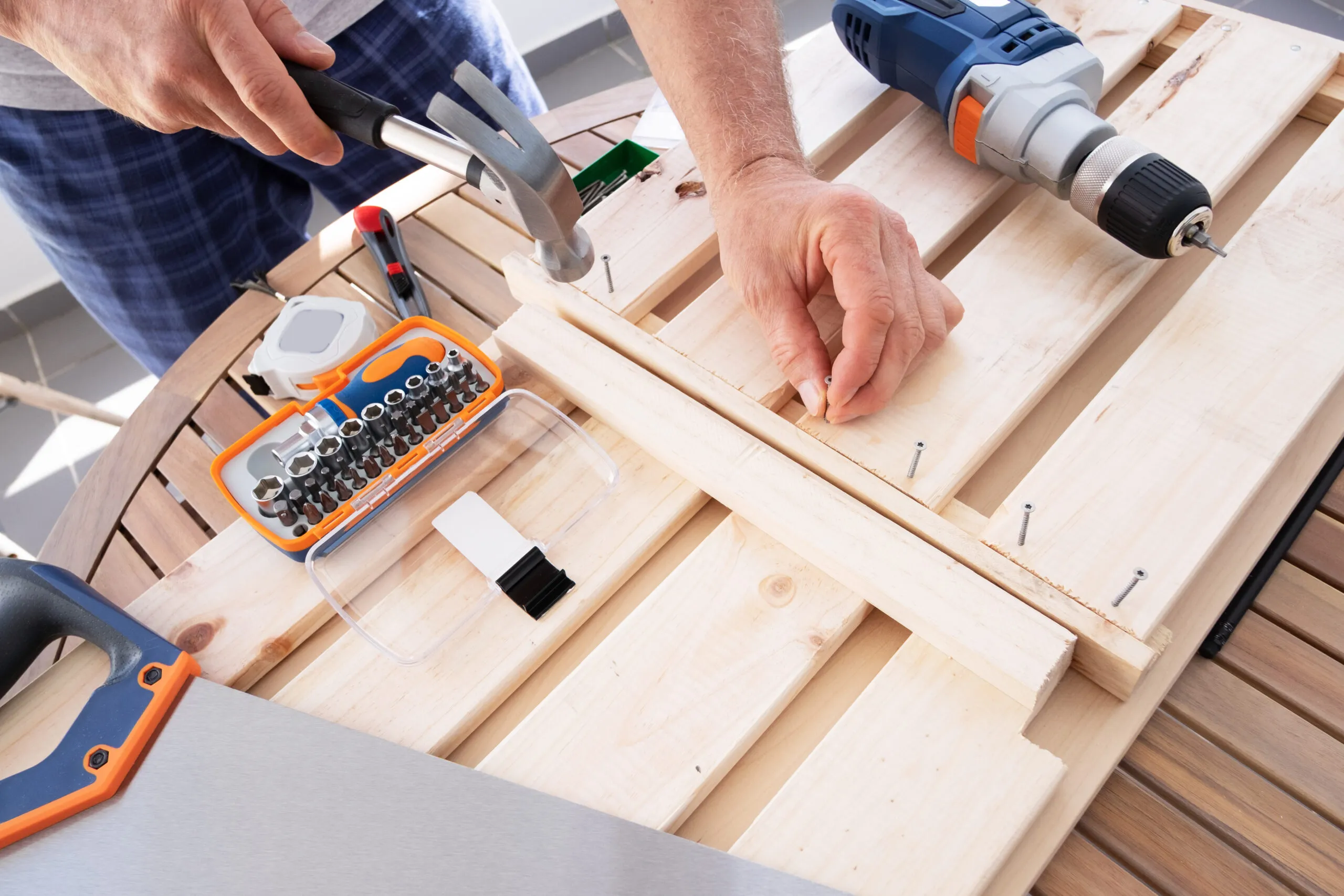 Hands driving nail with hammer into wooden shelf laying on round table.