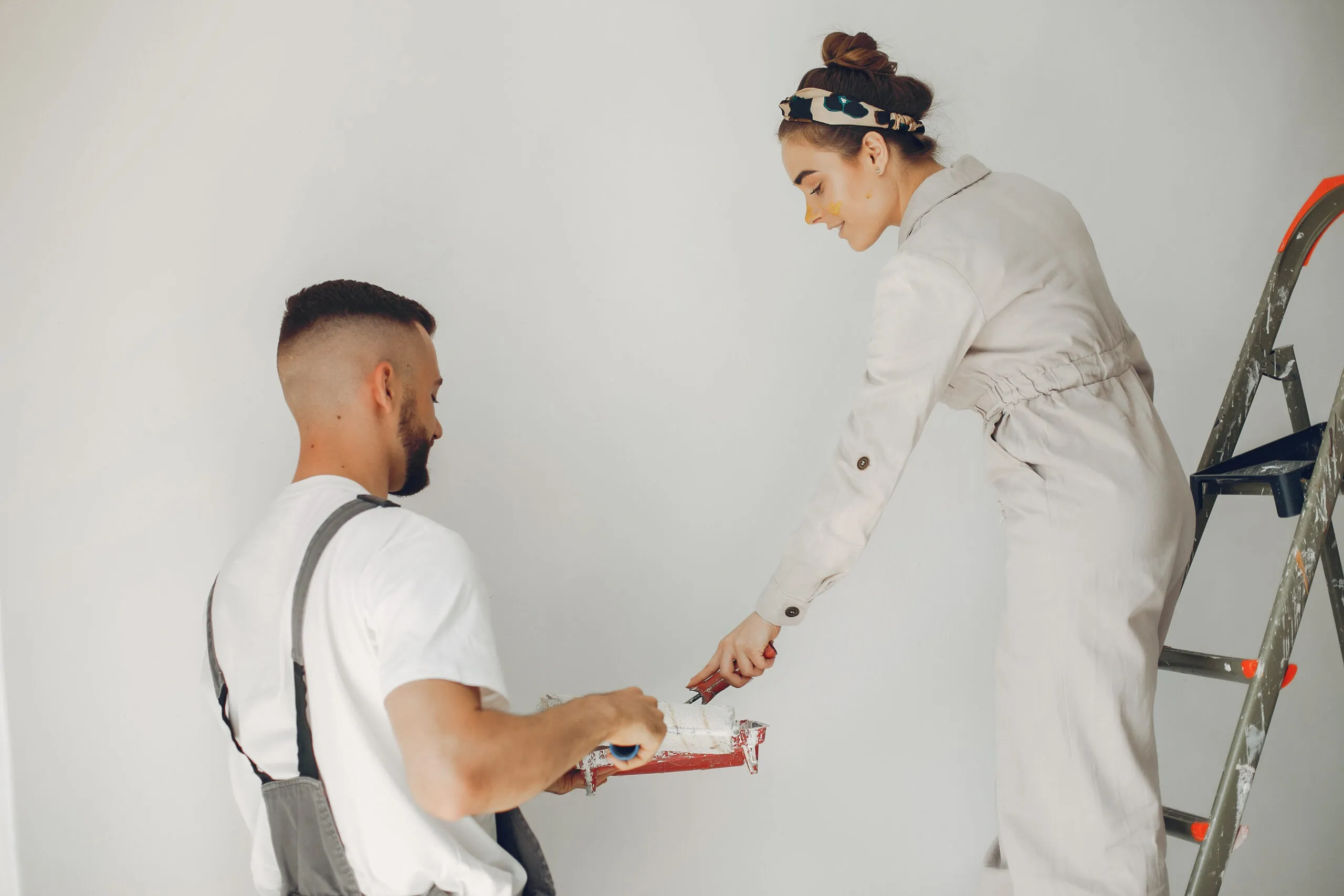 Family repairs. Couple at home. Woman in a overalls painting a wall.