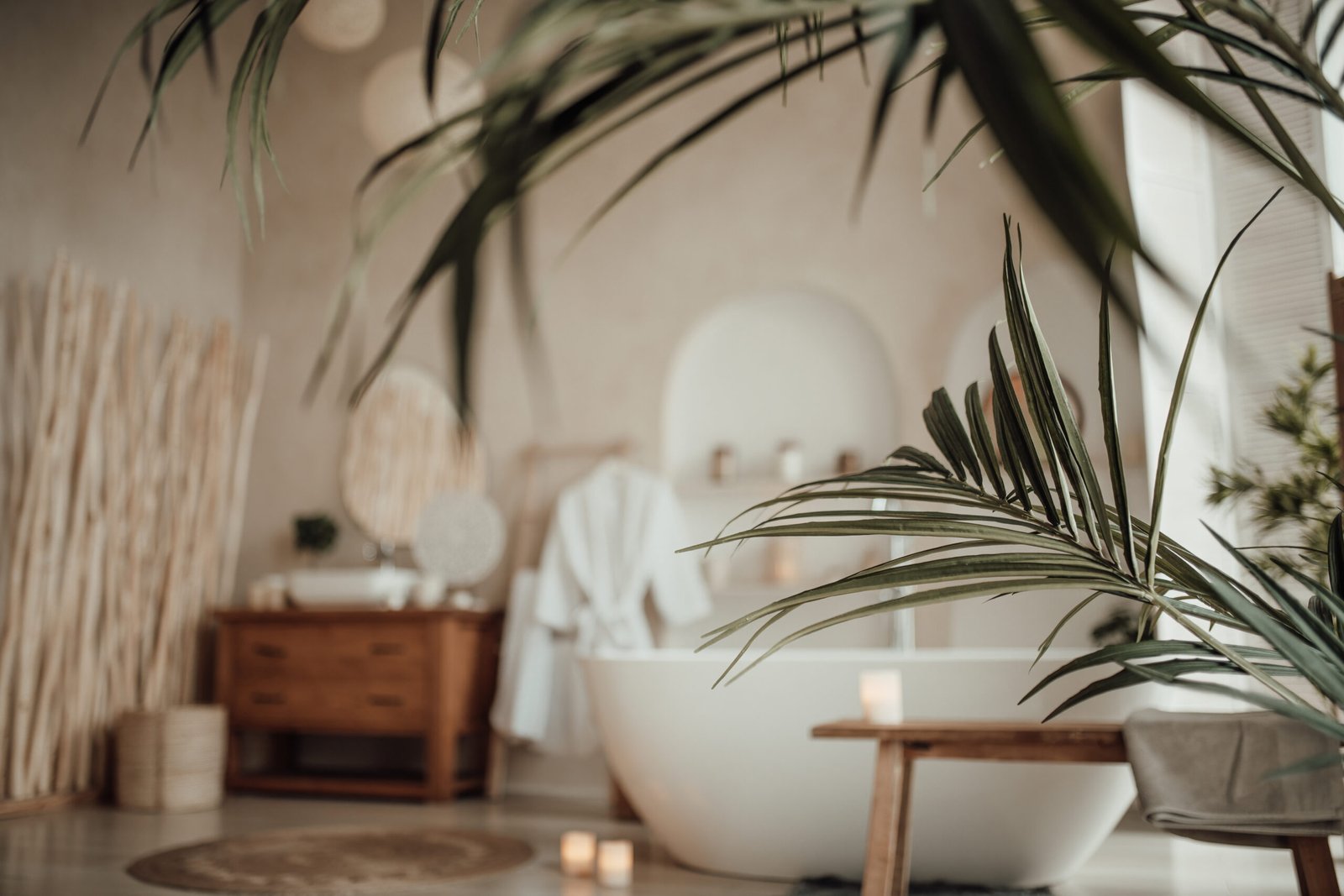Soft native hues organic shapes look of bathroom with big window oval bathtub in neutrals tones. Green palm plants candles bubblebath leasure and relaxation skin selfcare wellness luxury living.
