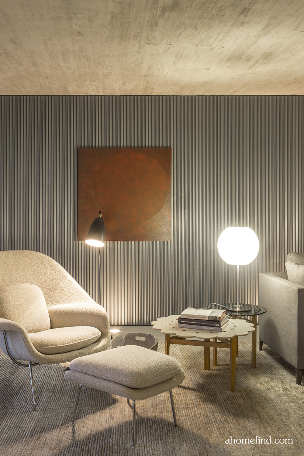 A white armchair with a stool and a coffee table. A floor lamp and a wall art on the panel wall. 