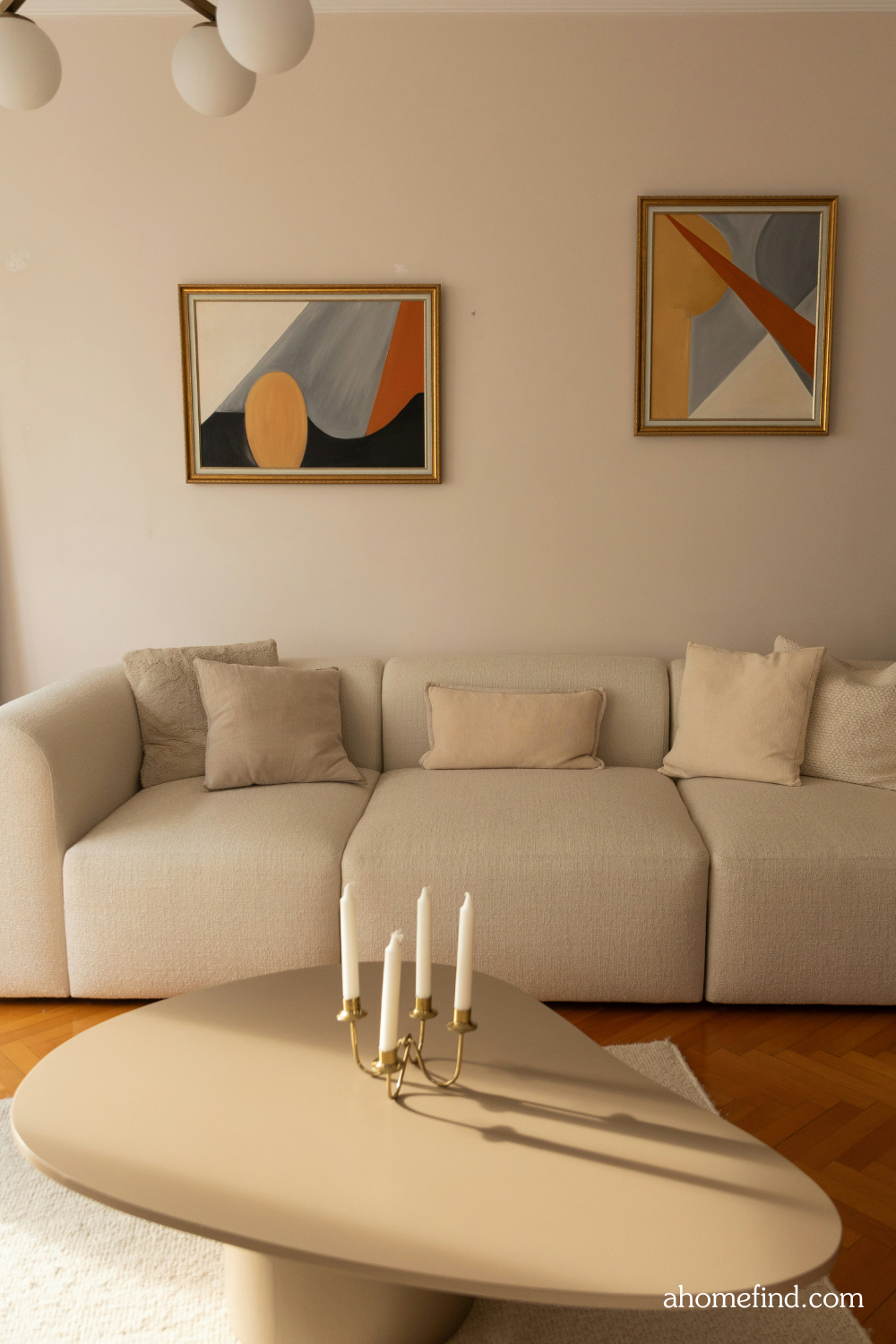 A clean mid century mdoern living room with a white sofa and a wound coffee table with a candle holder on it. Scaled. 