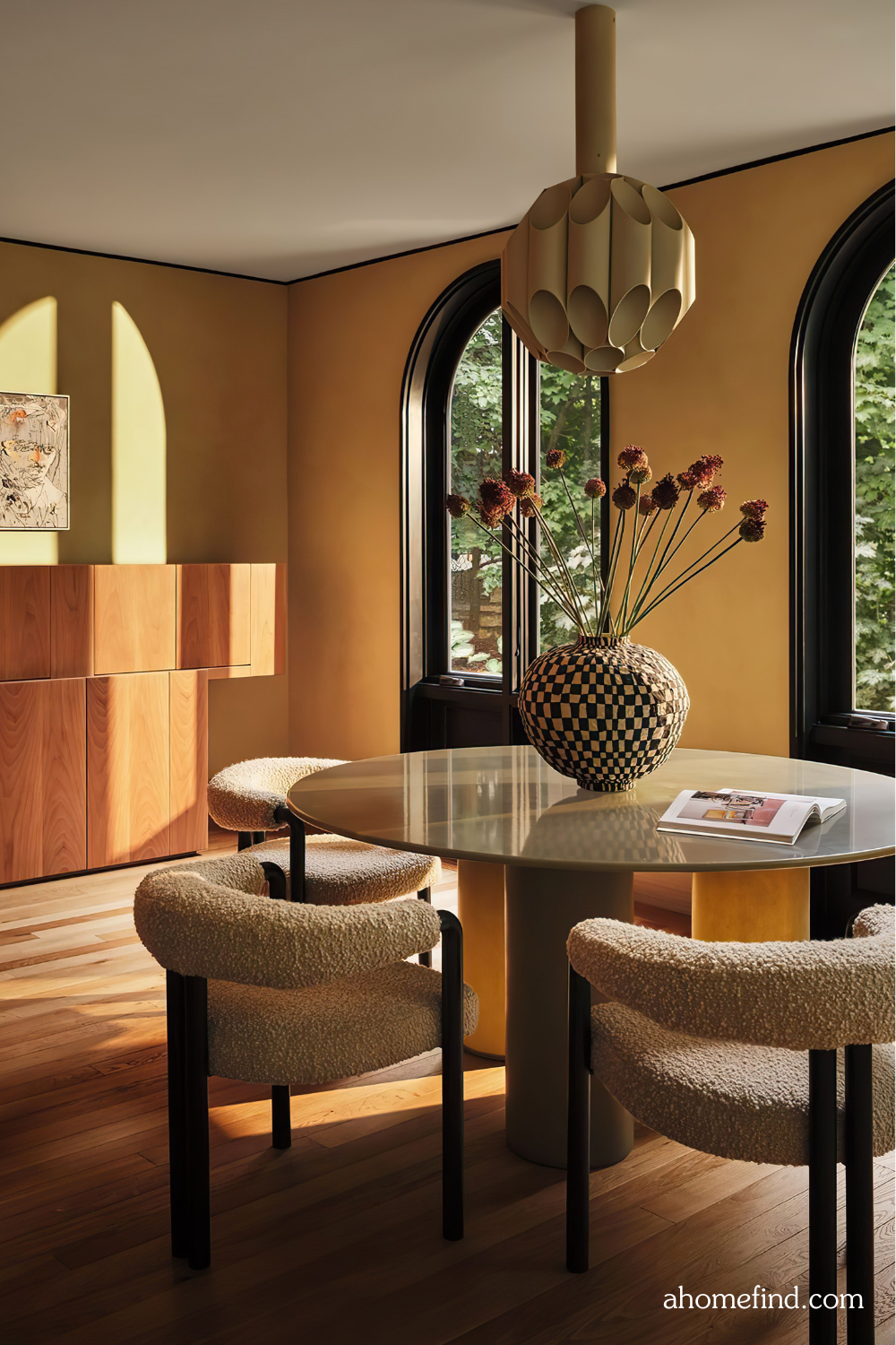 A mid century modern dining room with a glass table and beautiful chairs. A vase with flowers in the middle of the table. Scaled. 