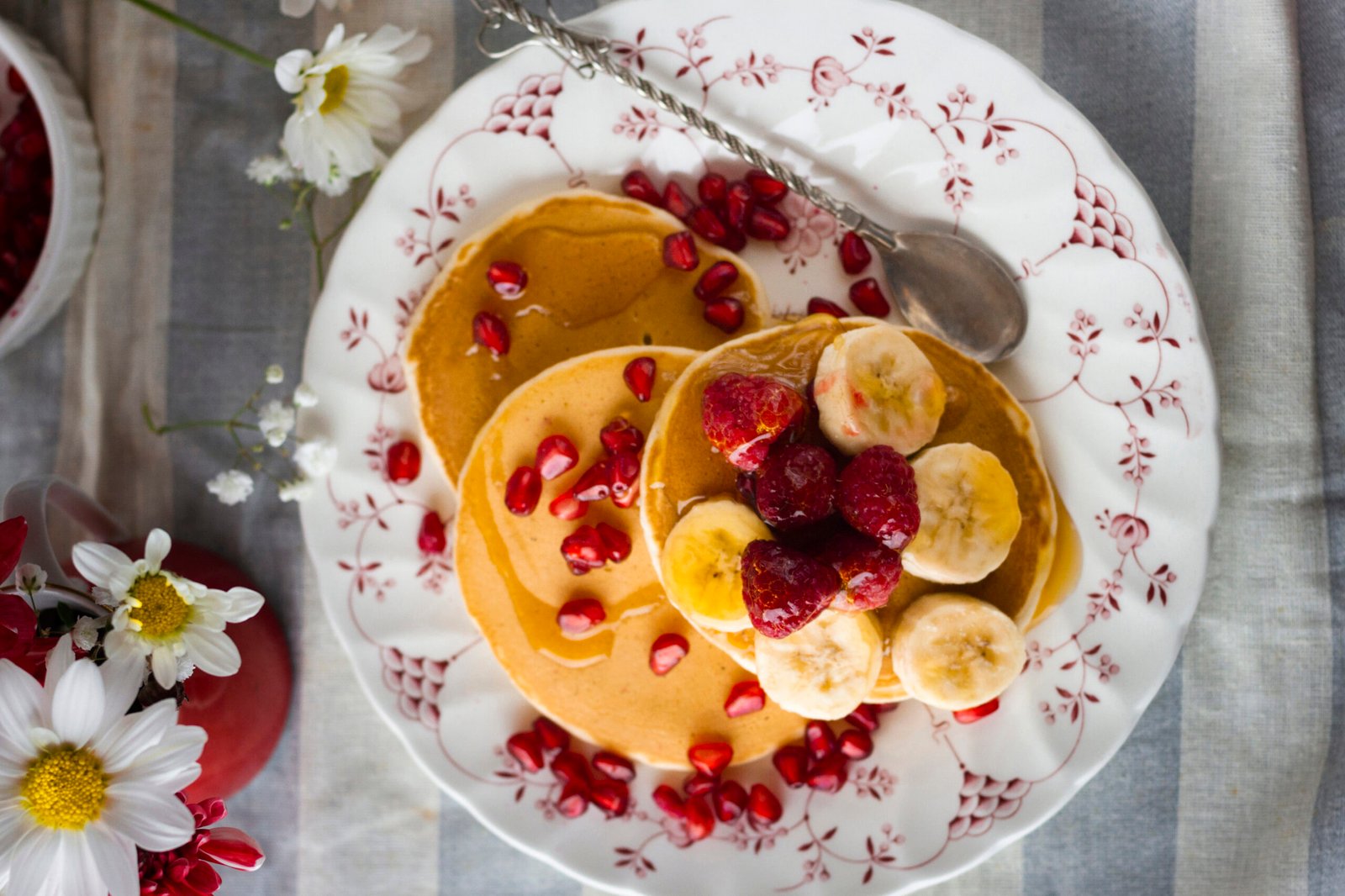 Floral plate with pancakes with pomegranate seeds, bananas and raspberries.