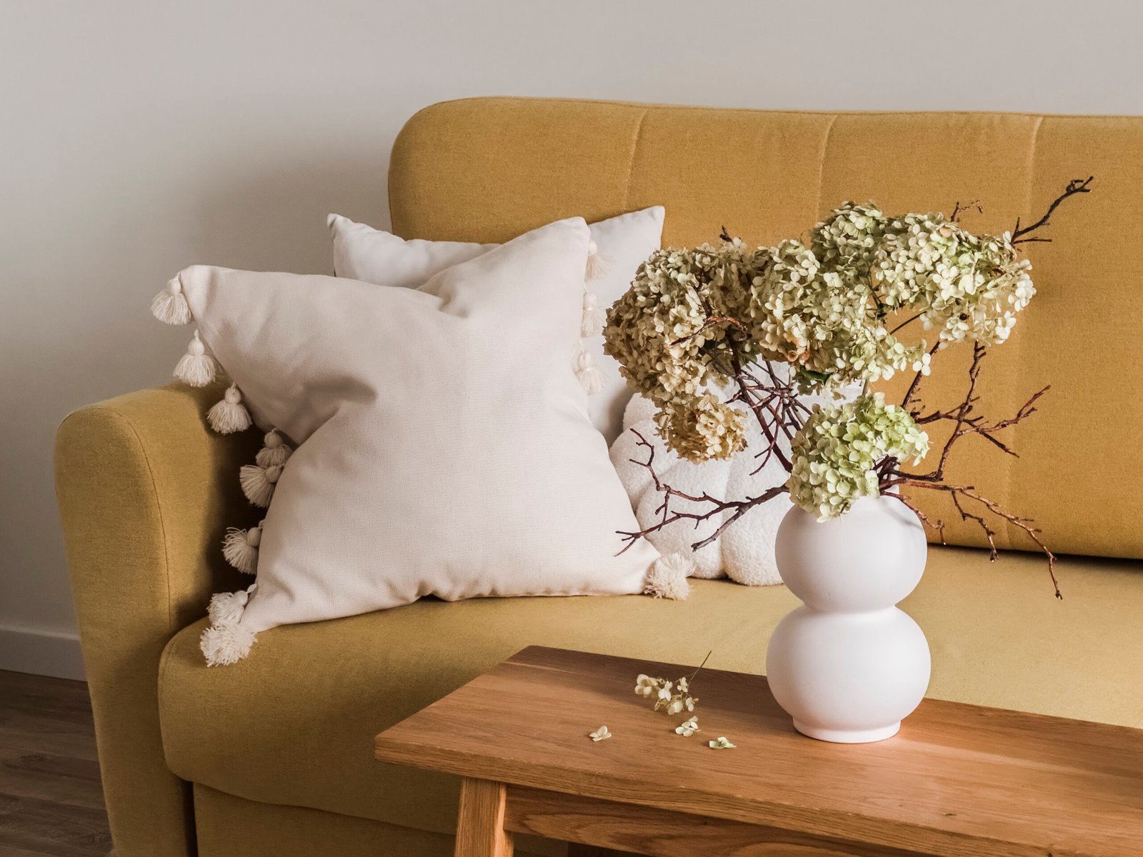A yellow sofa with decorative pillows, a wooden bench with a vase of dried hydrangeas in the living room.