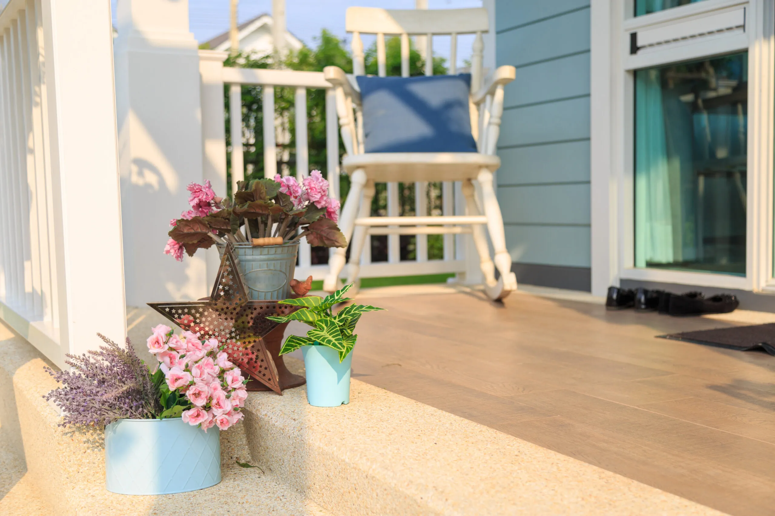 Pink flower bouquet in a blue pot and plant with a white wooden rocking chair on wooden floor in balcony with nature and sky background.