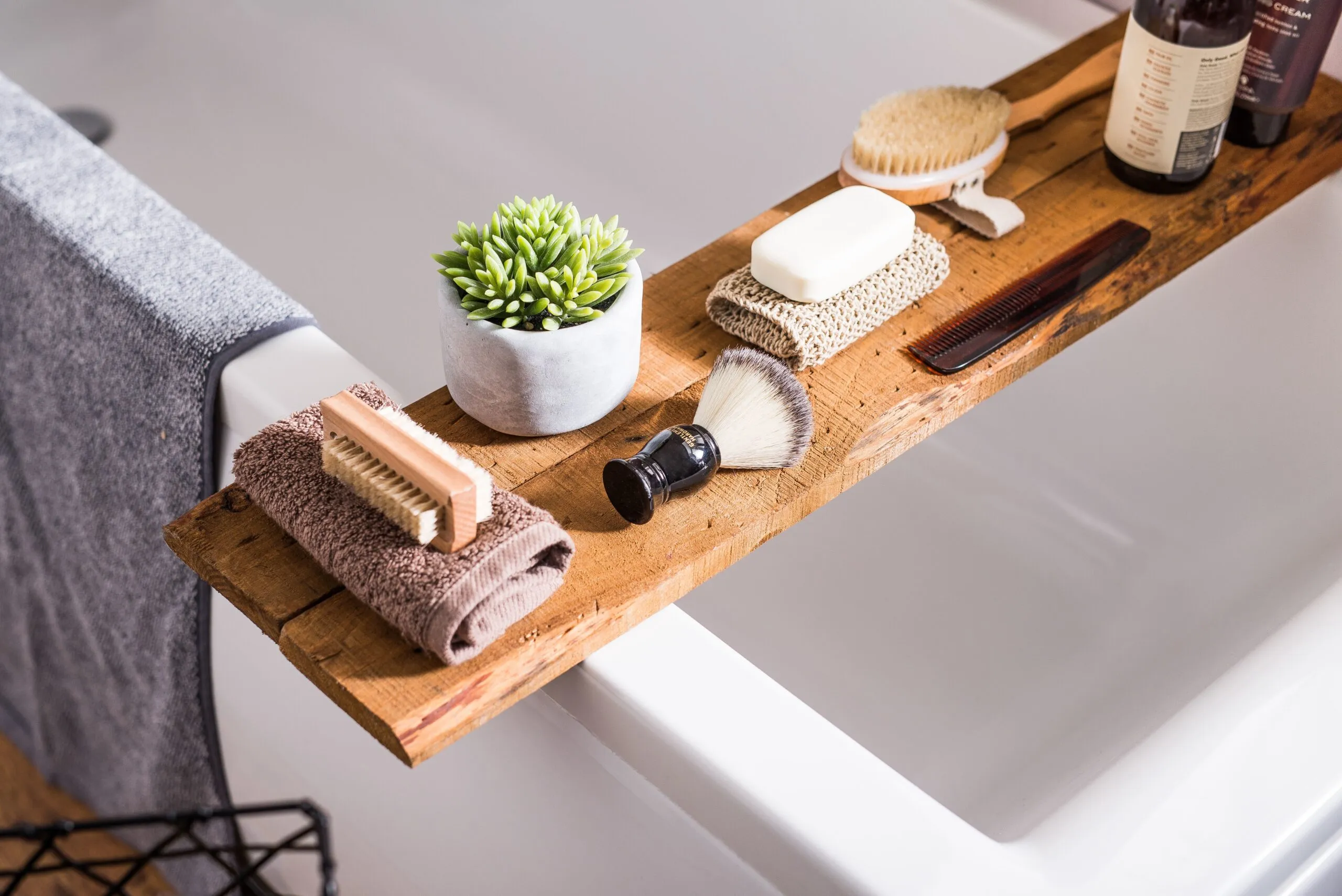A collection of bathroom equipment towels, shaving brush, hairbrush, shampoos and soap on a wood.
