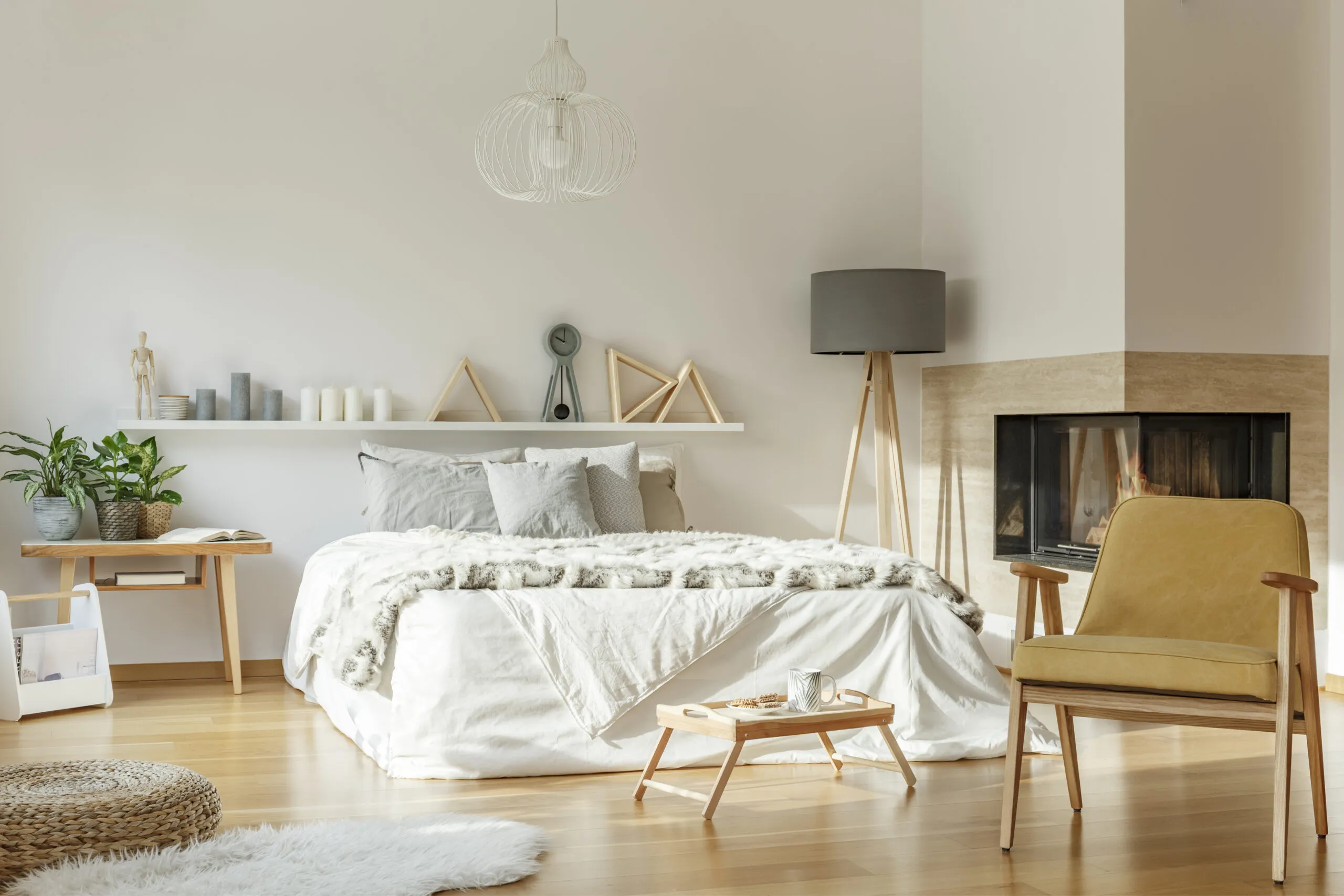 Cozy bedroom interior with fireplace, king-size bed, rug, chair, lamp, ornaments and wooden floor.