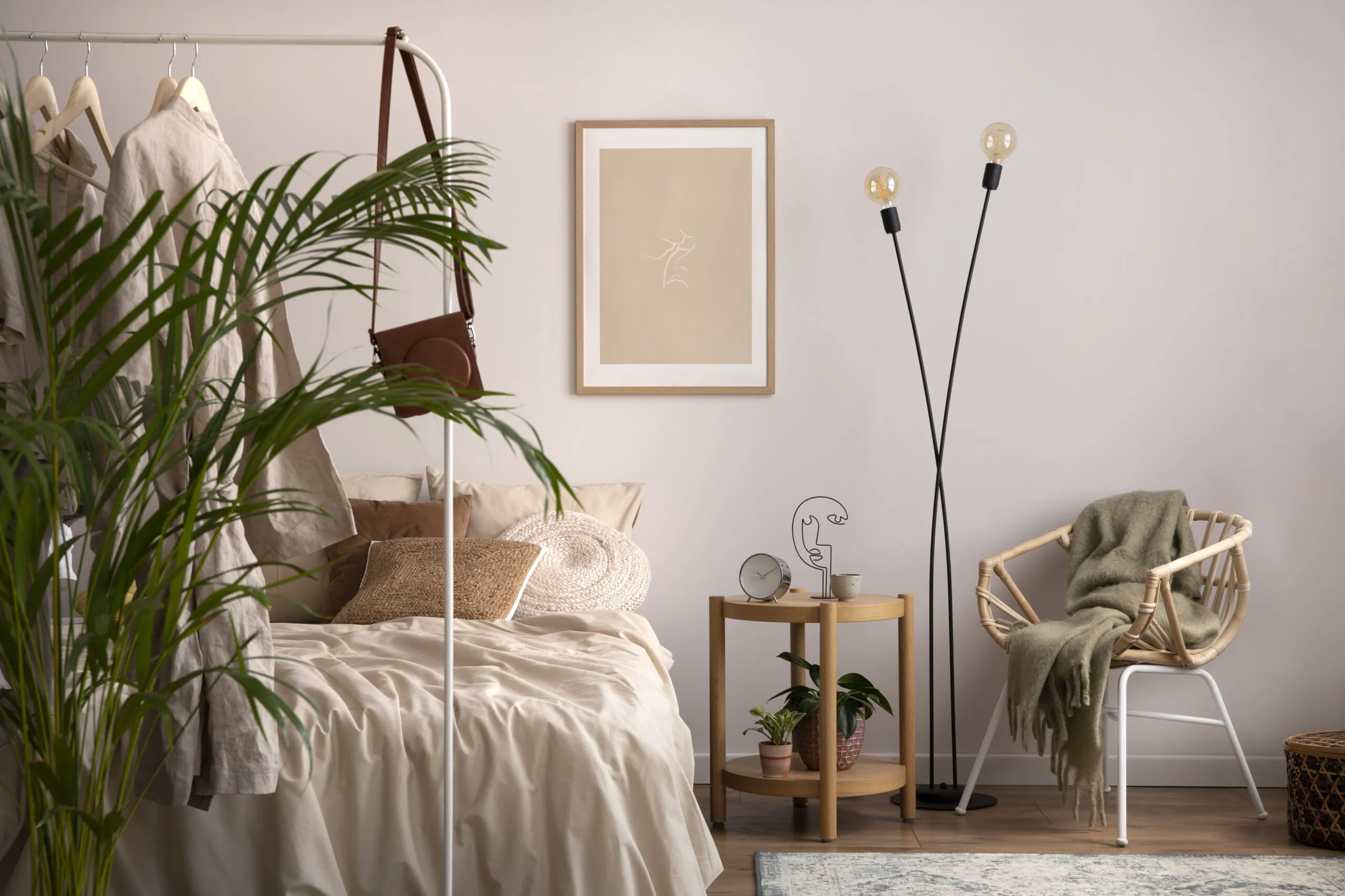 Stylish composition of cozy bedroom with mock up, beige bedding, plants, armchair and wooden coffee table. 