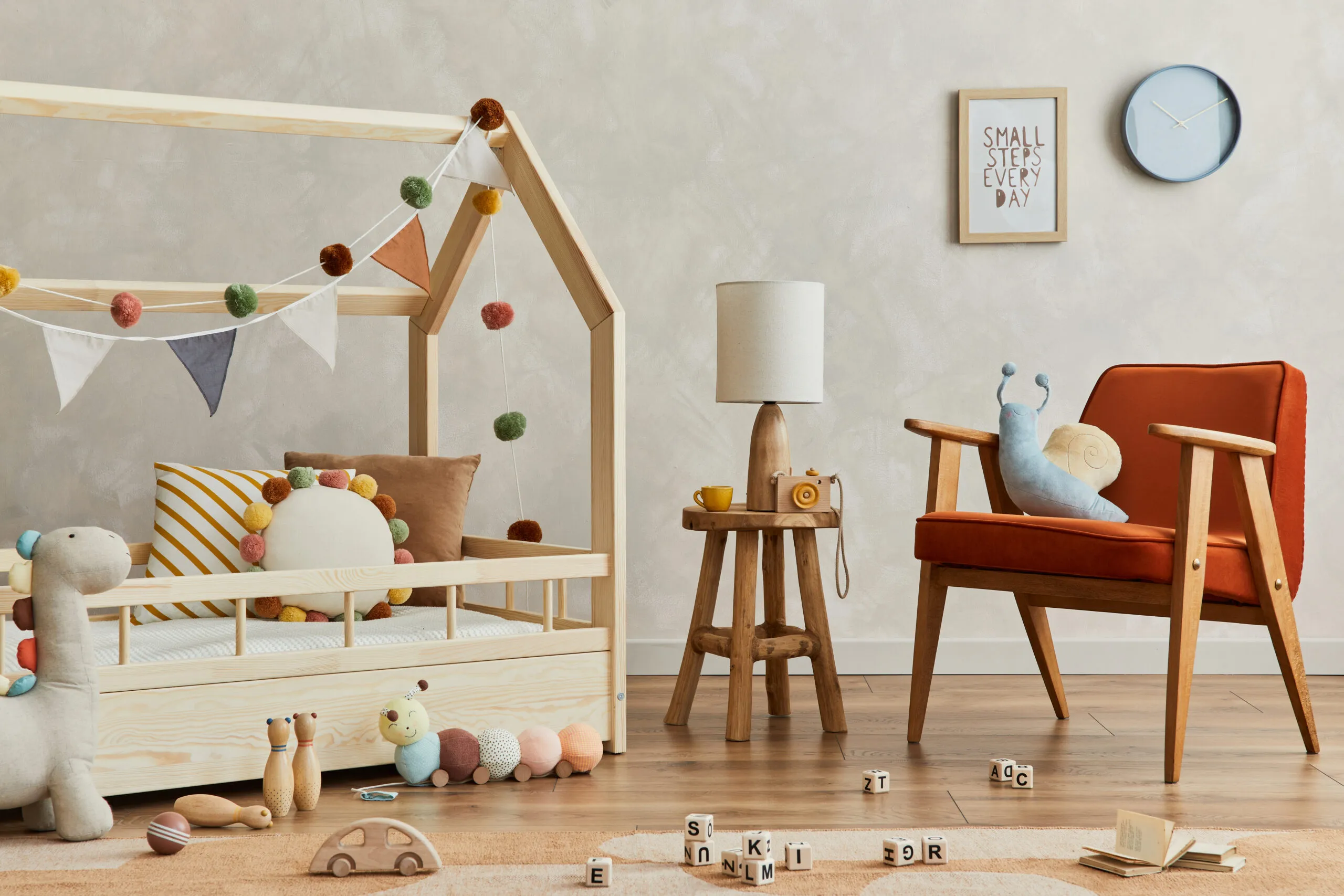 Stylish composition of cozy scandinavian child's room interior with wooden bed, red armchair, plush and wooden toys and textile hanging decorations.