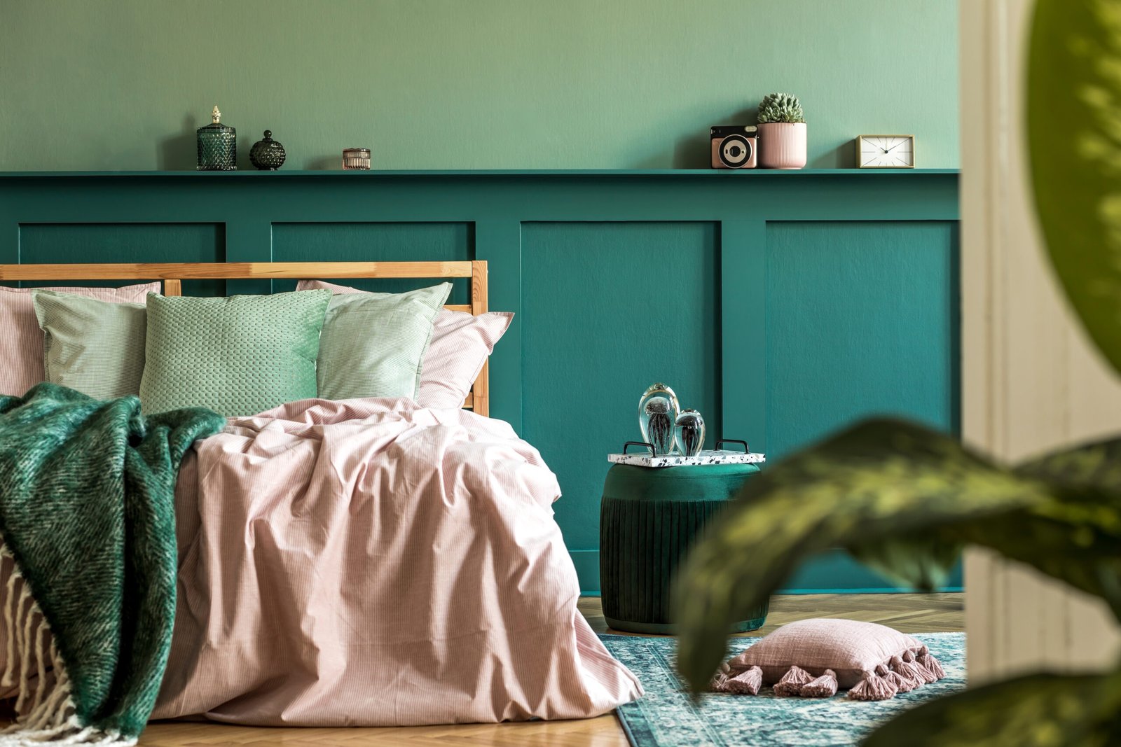 Stylish interior design of bedroom with modern furnitures, plants and elegant accessories. Shelf above the bed. Beautiful pink and green bed sheets, blankets and pillows. 