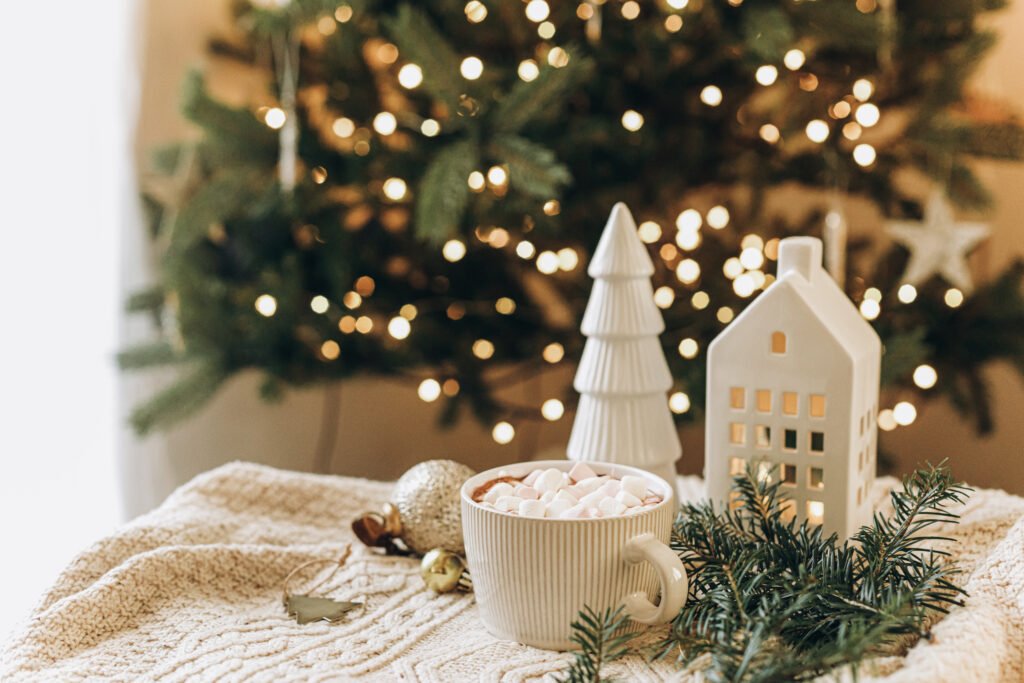 Christmas background. Cup of hot chocolate with marshmallows, christmas ornaments, cozy knitted sweater and fir branches against stylish tree with lights.