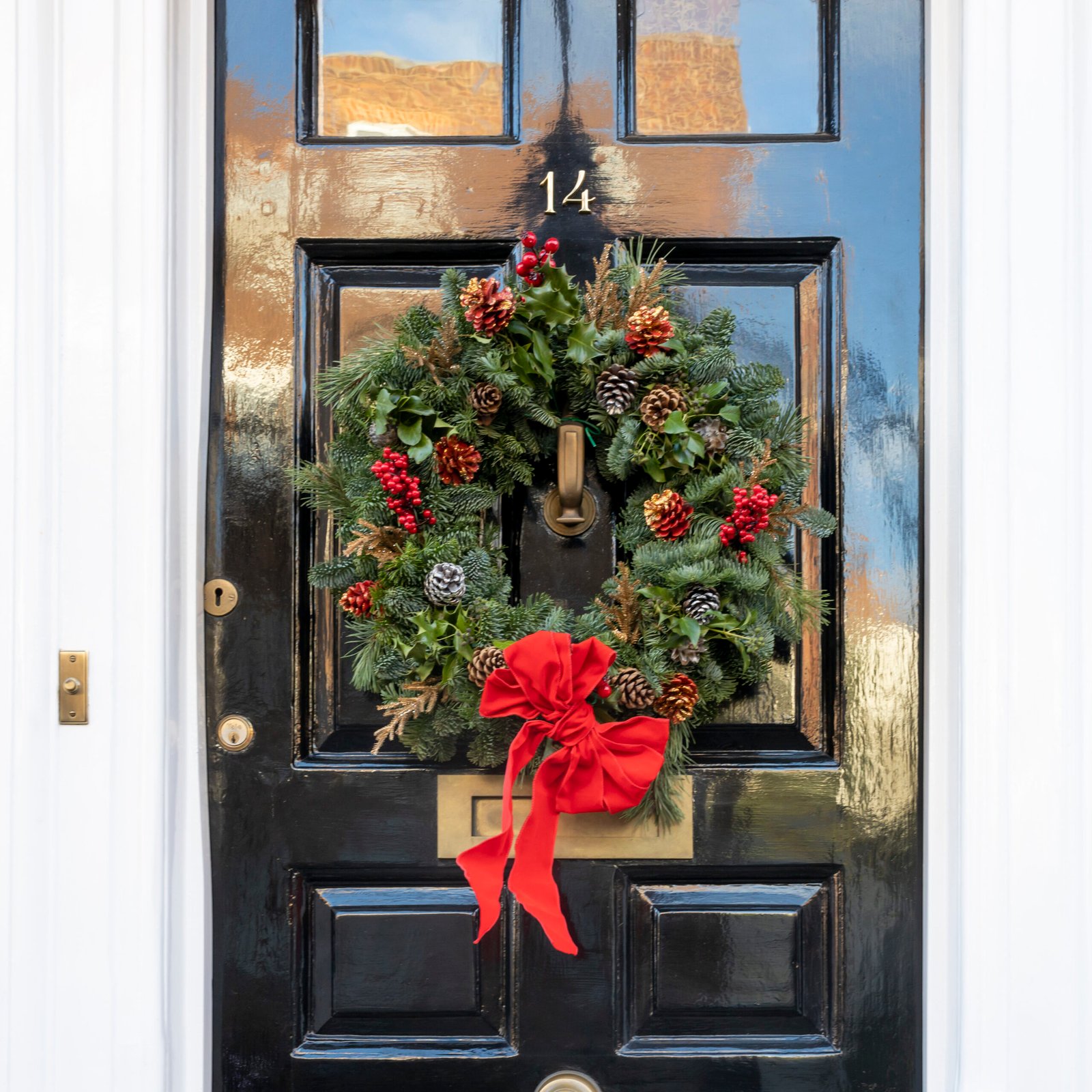 Christmas wreath made of fir branches, pine cones, red viburnum berries and a bow on a black London door.