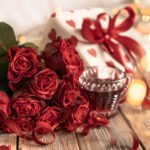 Cozy composition for Valentine's Day with a bouquet of red roses and a red drink in a cup on a wooden background.