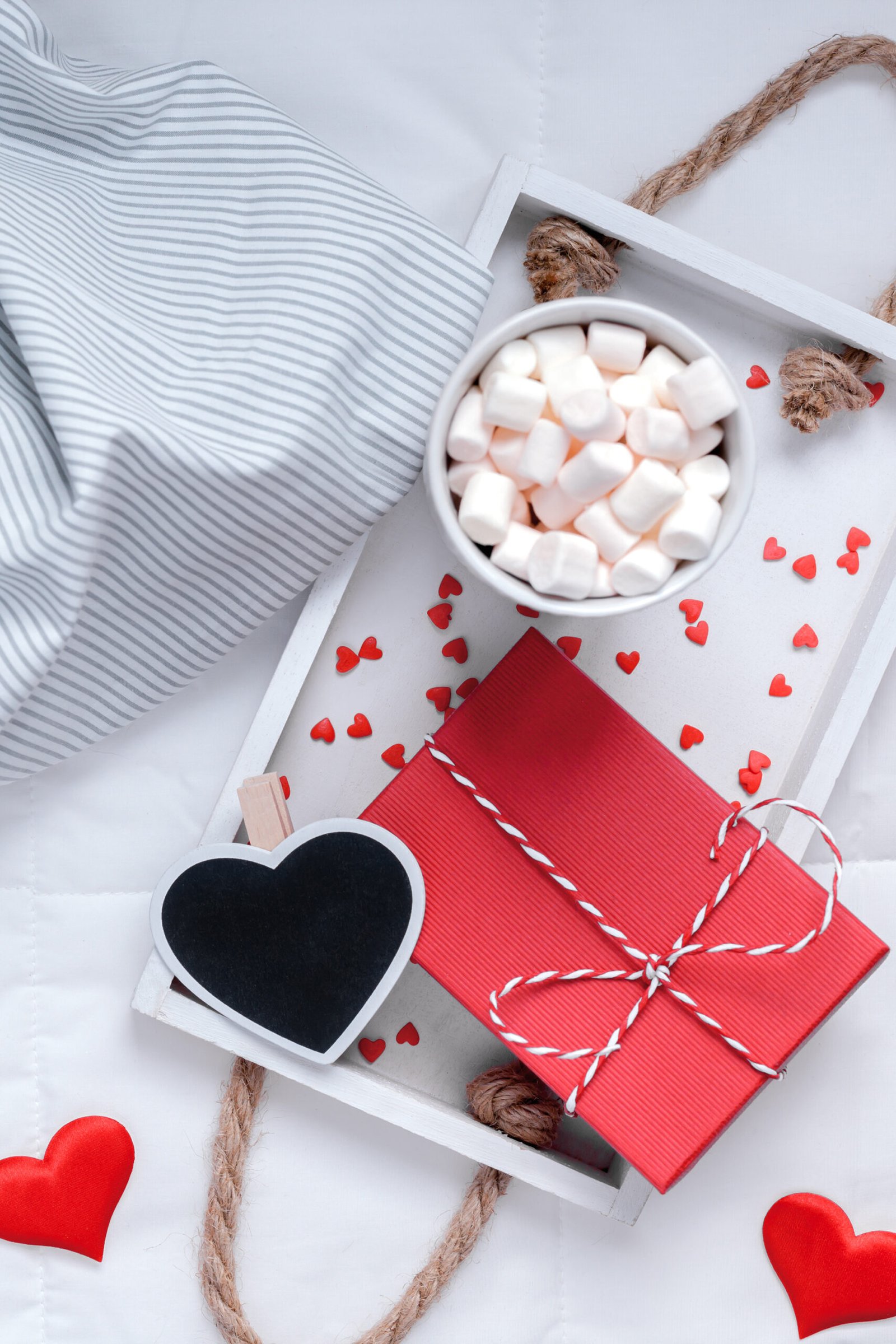 Creative Top view flat lay sill life romantic composition. Hot cacao coffee chocolate with marshmallows mug red gift hearts tray in bed. Concept Valentine holiday cozy warm home morning natural light