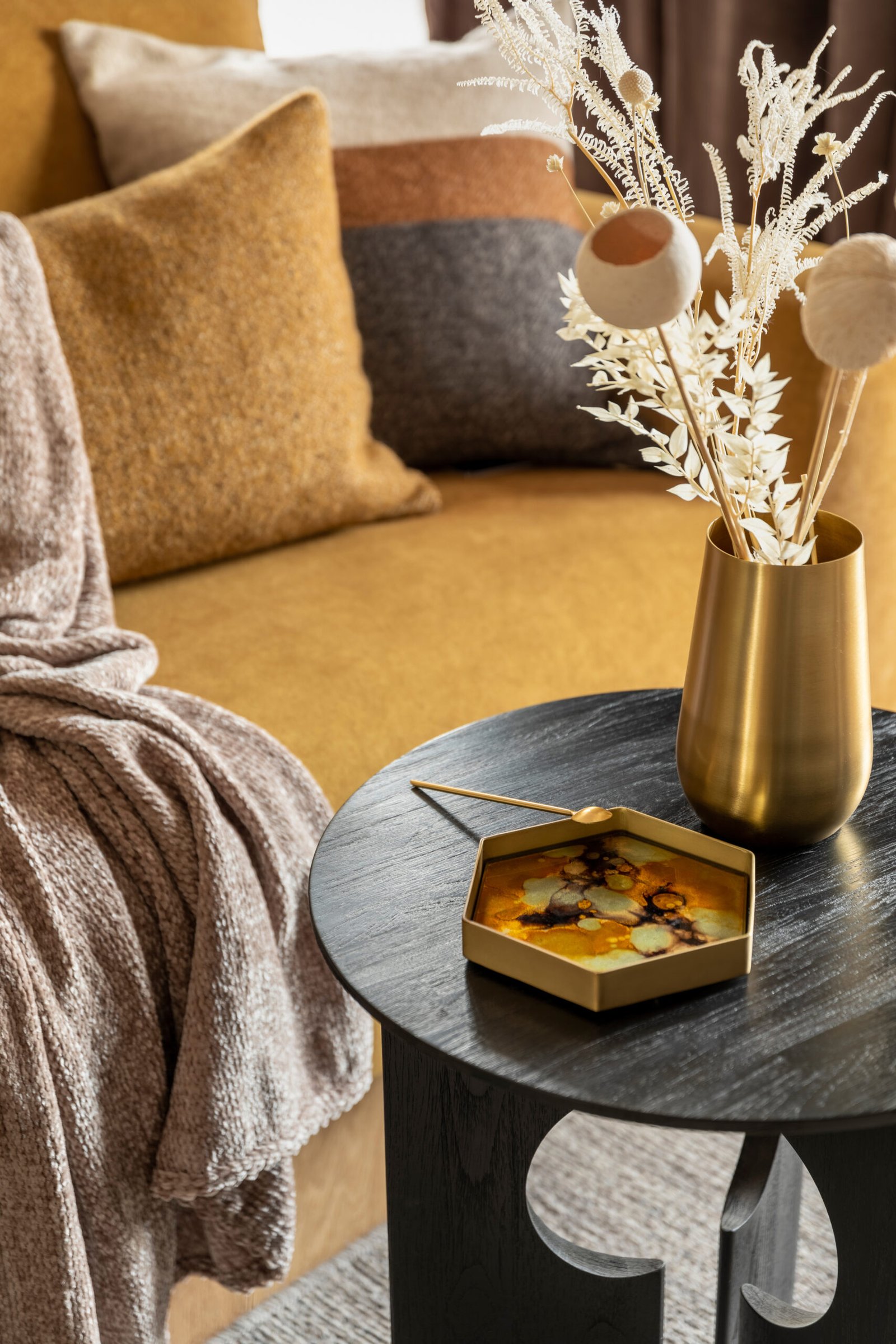 Stylish composition of modern living room. Stylish coffee table with tray and gold vase with dried flowers. Yellow sofa with plaid and pillows. 