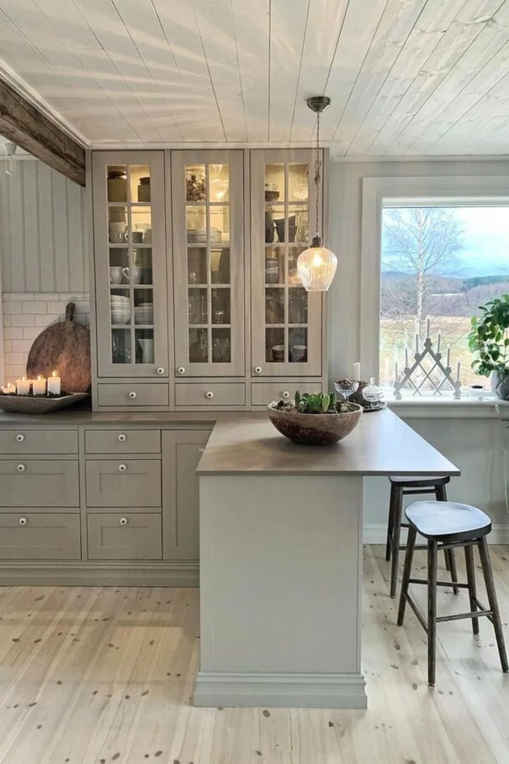 Swedish farmhouse style kitchen with green cabinets, a wooden countertop and barstools. Kitchen cabinets with glass doors.