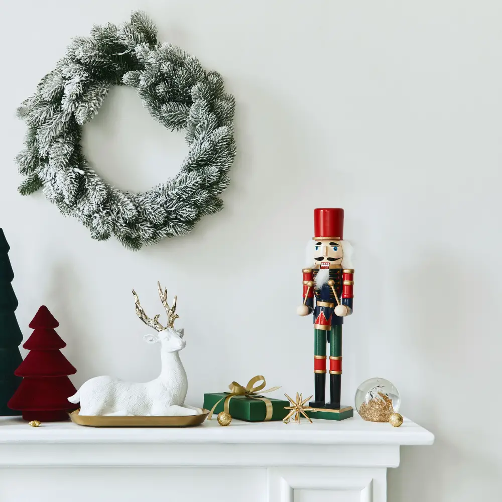 A fireplace with a nut cracker and a reindeer on it. Above it hangs a wreath.