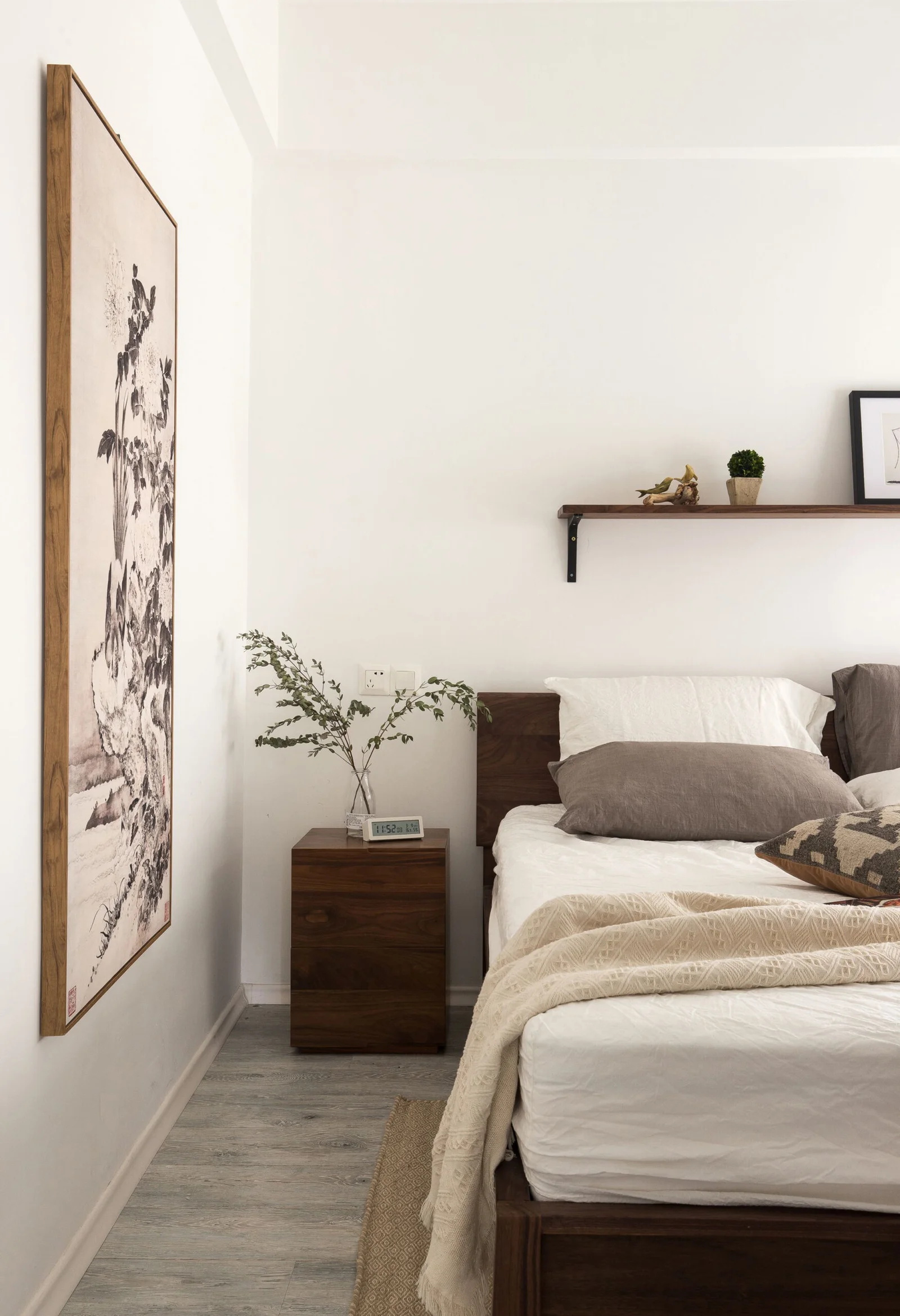 Bedroom with dark wooden bed frame and bedside table. An open shelf with decorative picks on it. A large wall art.