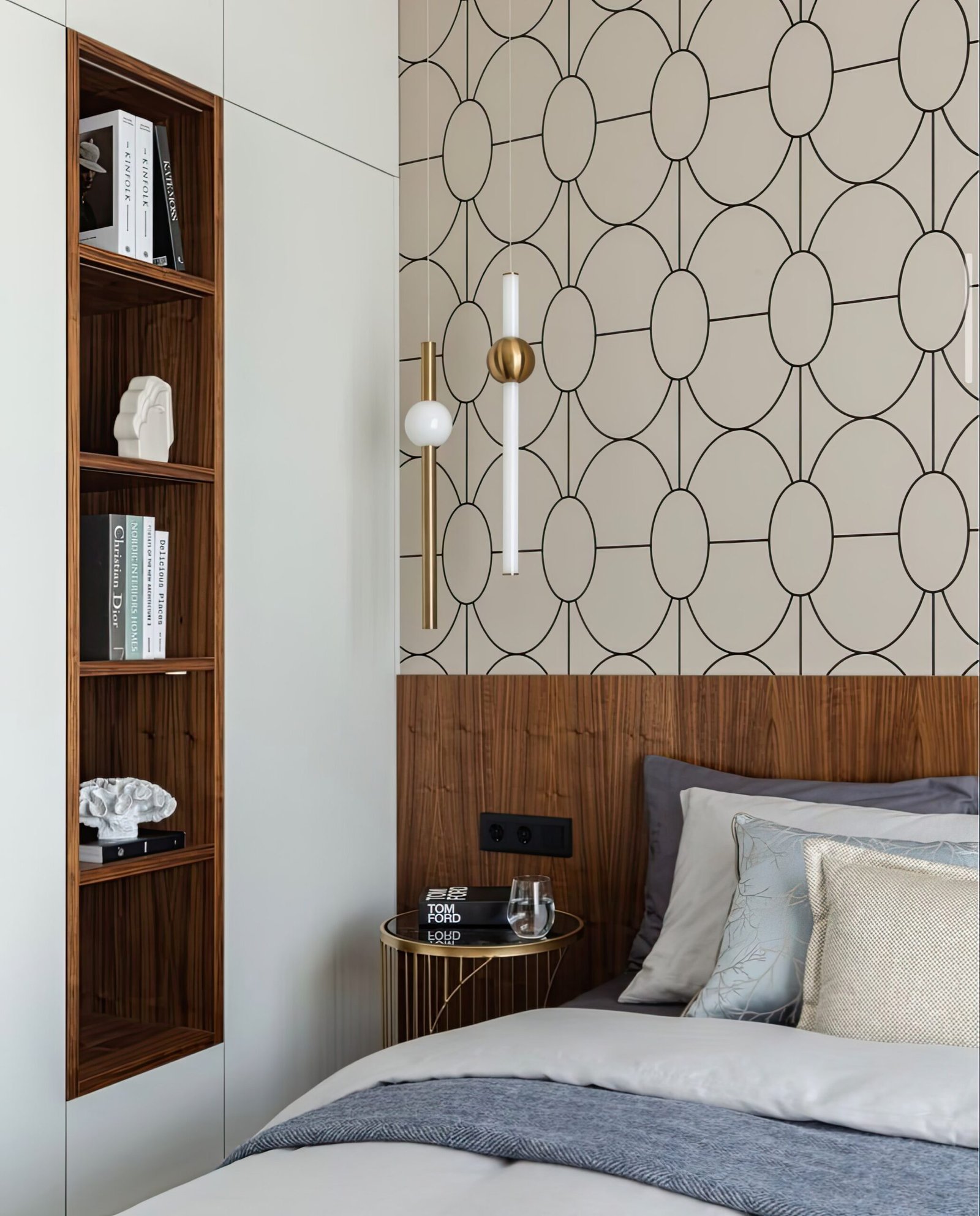 Bedroom with an accent wall paper wall, wooden panels and a light on the wall. Built in shelves. Bed with bedding. 