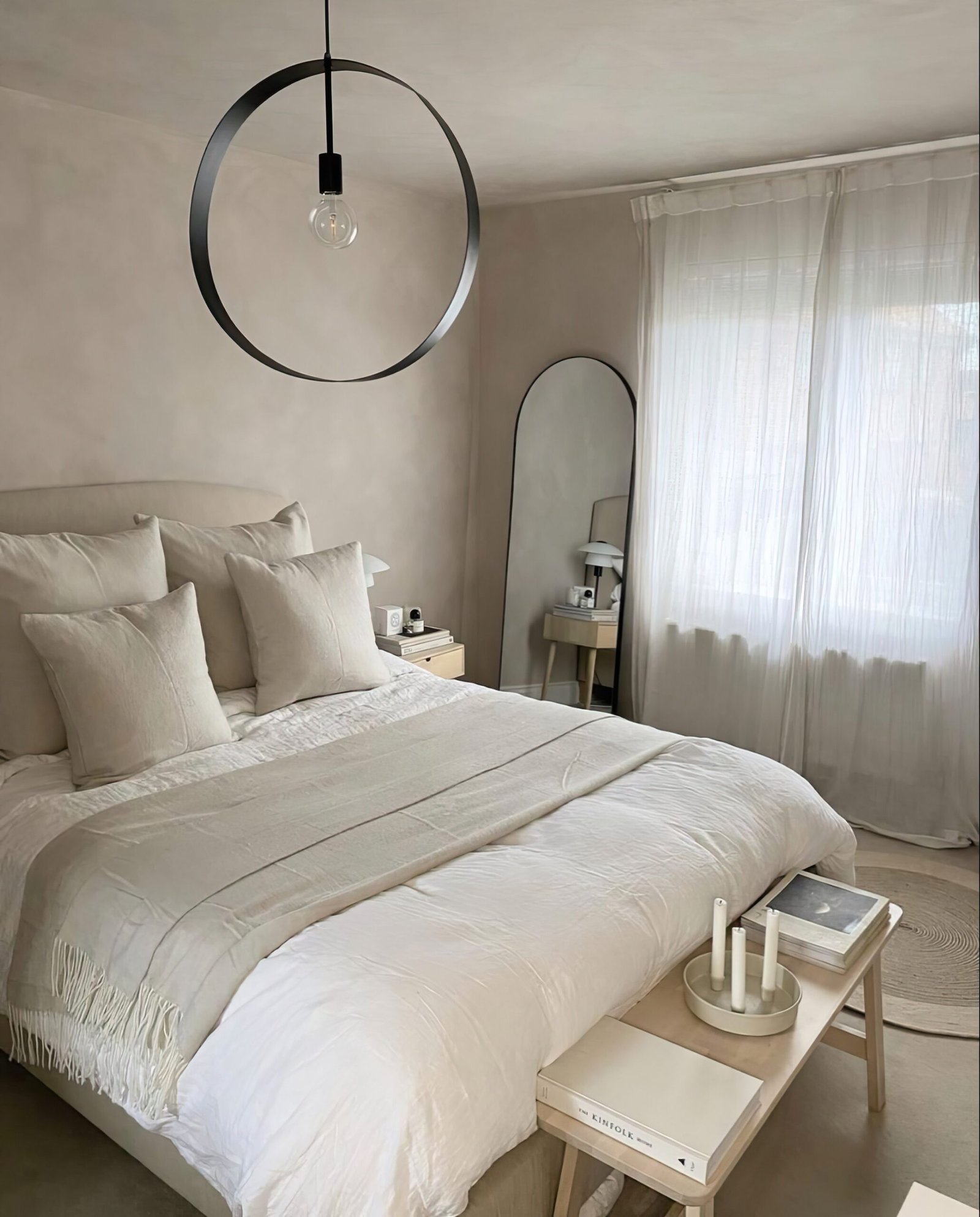 Neutral bedroom ideas with a white bedding, a black framed mirror, a black ceiling lamp and wooden bench by the end of the bed. light white curtains. 