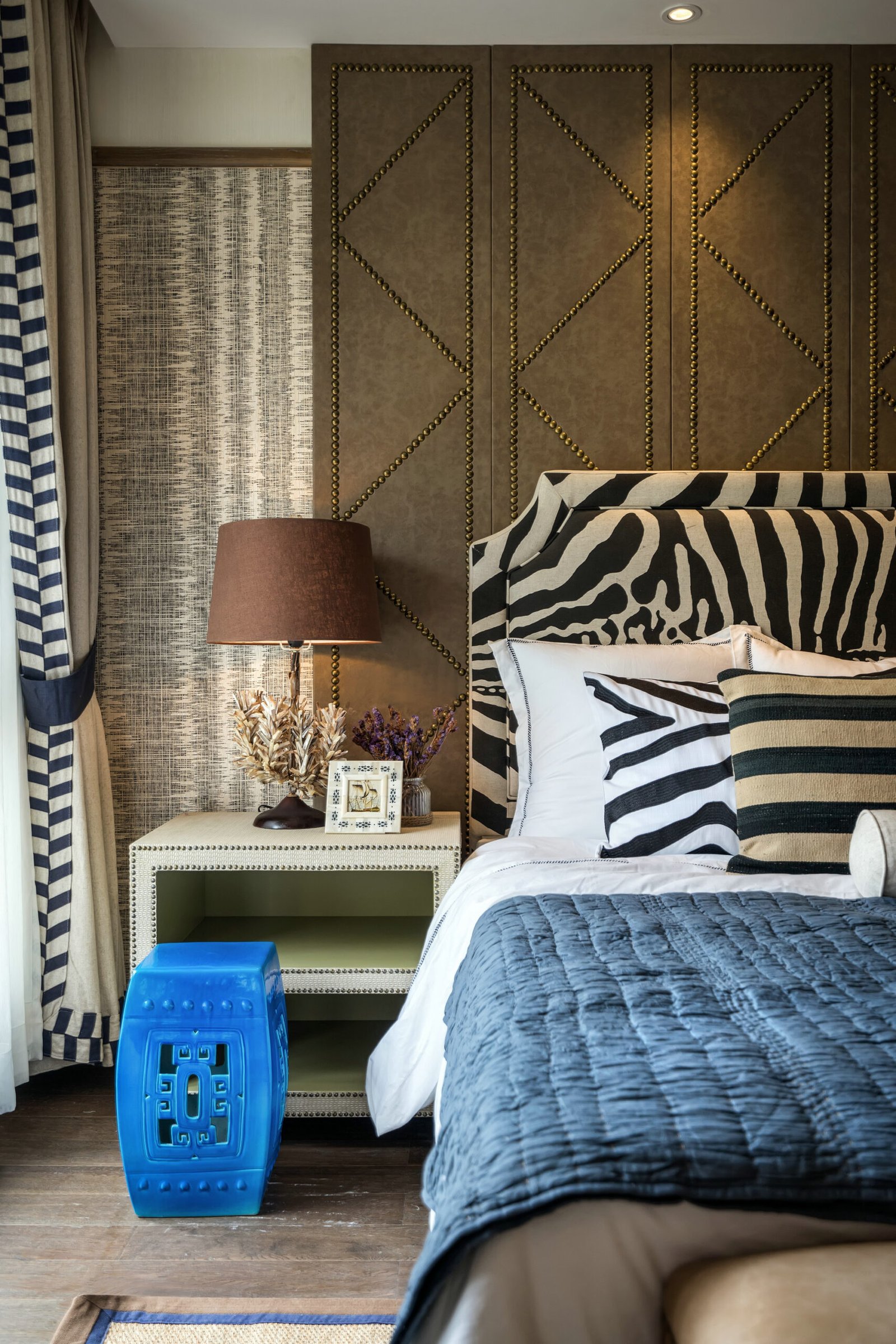 Bedroom with zebra bed and zebra pillows. A neutral bedside table with a table lamp and walls in a geometric pattern. 