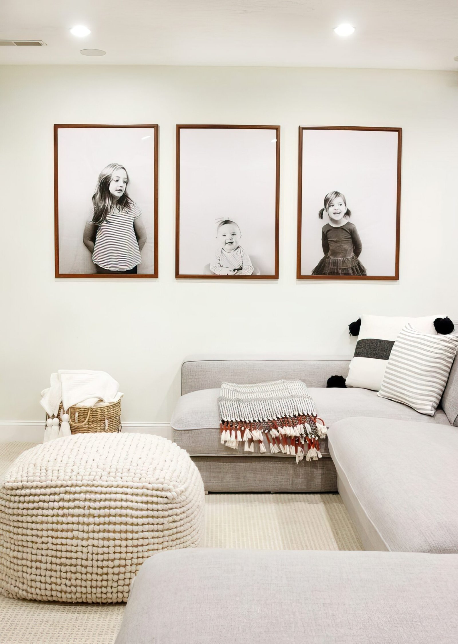 A large grey sofa with an ottoman in front of it. On the big wall is three framed photos of children.