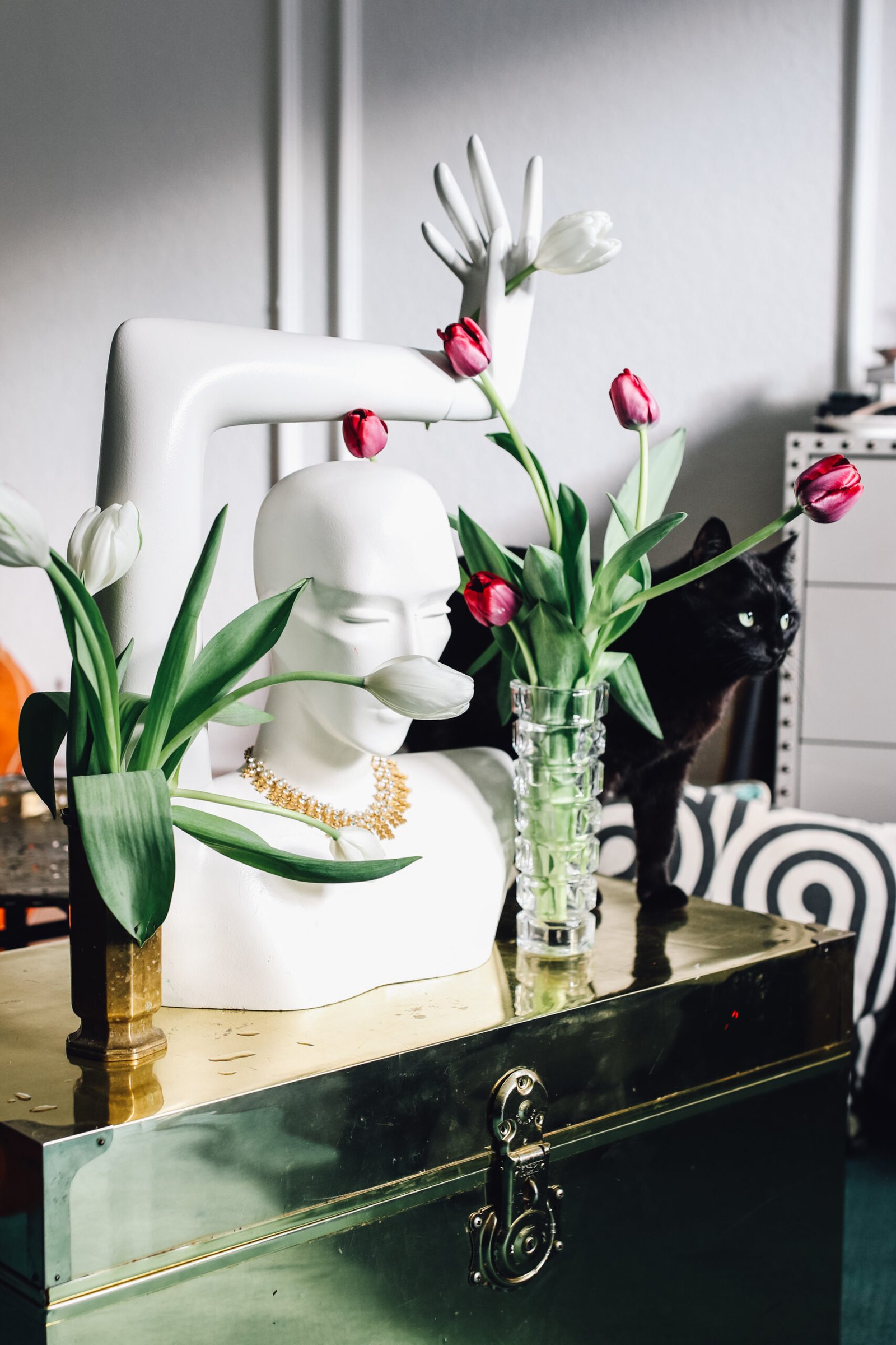 Glamorous mannequin with pink and white tulips and a black cat on top of an golden table. 