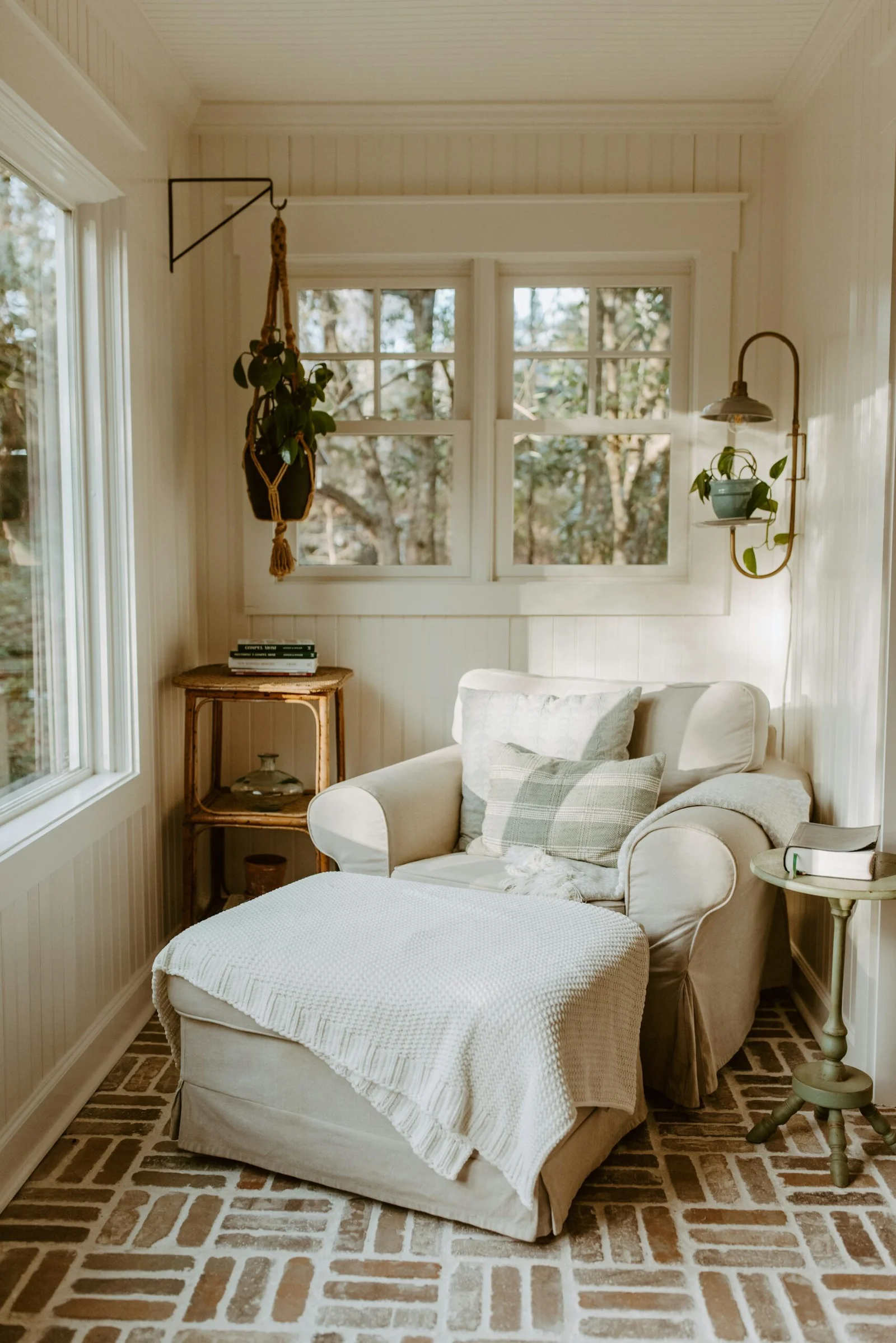 Home armchair in a corner with a window above it. A wall lamp hanging and plants. 