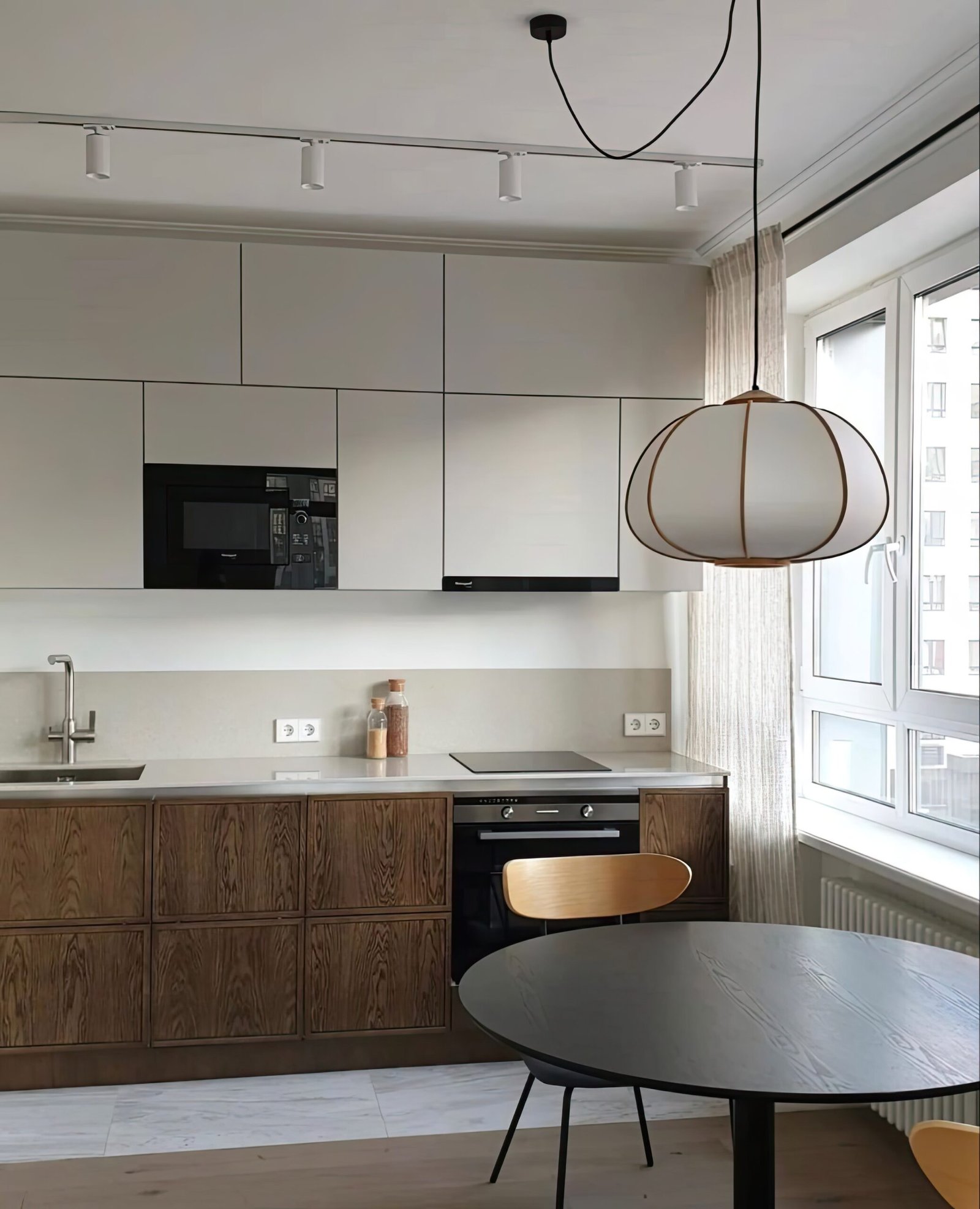 Japandi kitchen in wood with a white counter top. In front of the kitchen is a black dining table with a large ceiling lamp above it. 