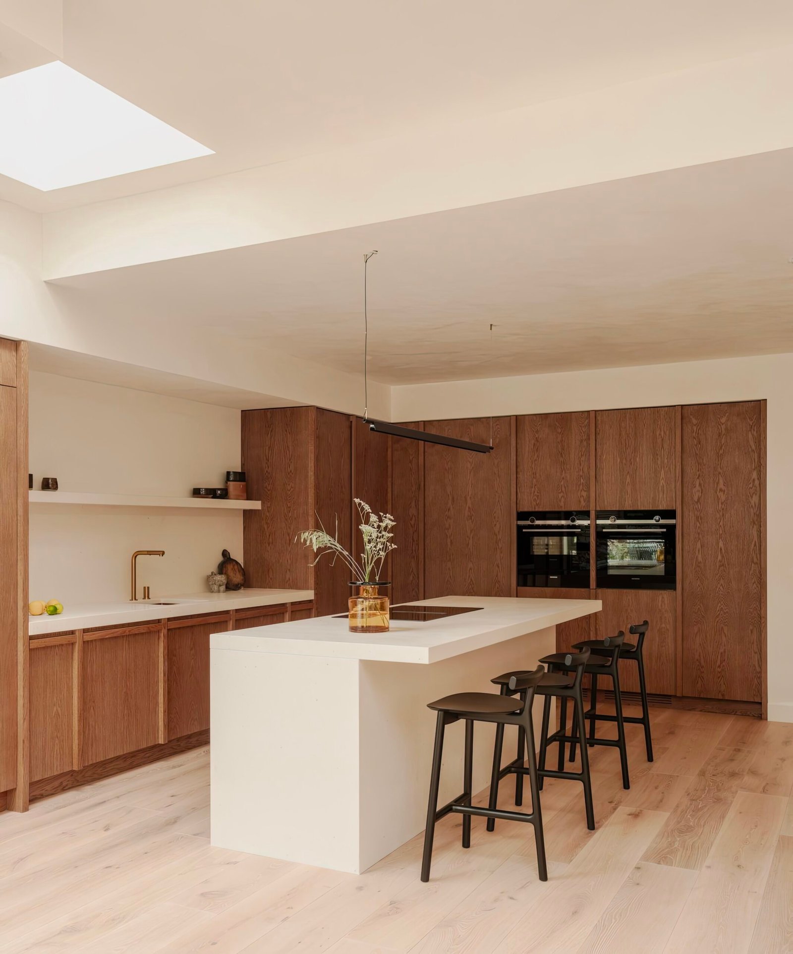 Kitchen with a white kitchen island. Kitchen counters are in wood with a white counter top. Wooden floor and wooden chairs. 