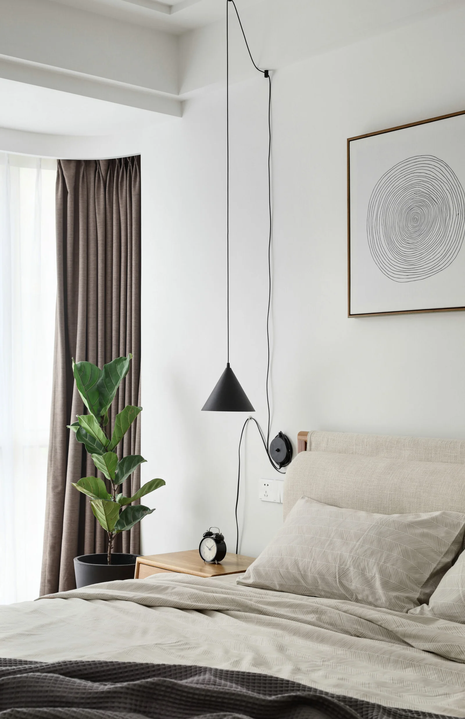 Room with plants and a hanging ceiling lamp. A neutral bedding and a wall art.