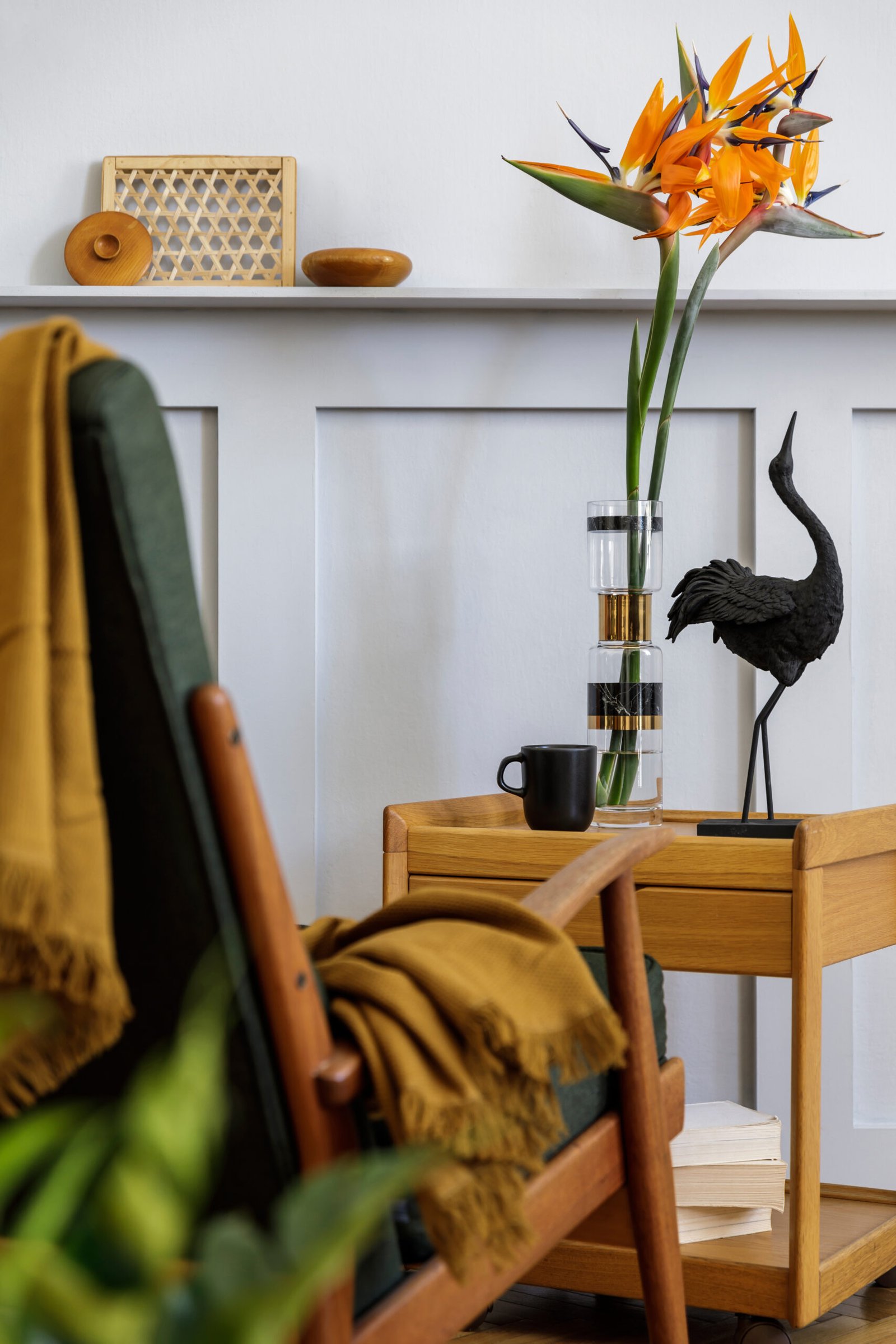 Stylish composition at living room interior with design armchair, plaid, plant, cup of coffee, flower in vase, book, wood panels with shelf and elegant presonal accessories in modern home decor.