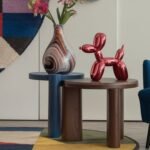 Colorful table with a vase with flowers in it, a red decorative dog and a blue accent chair.