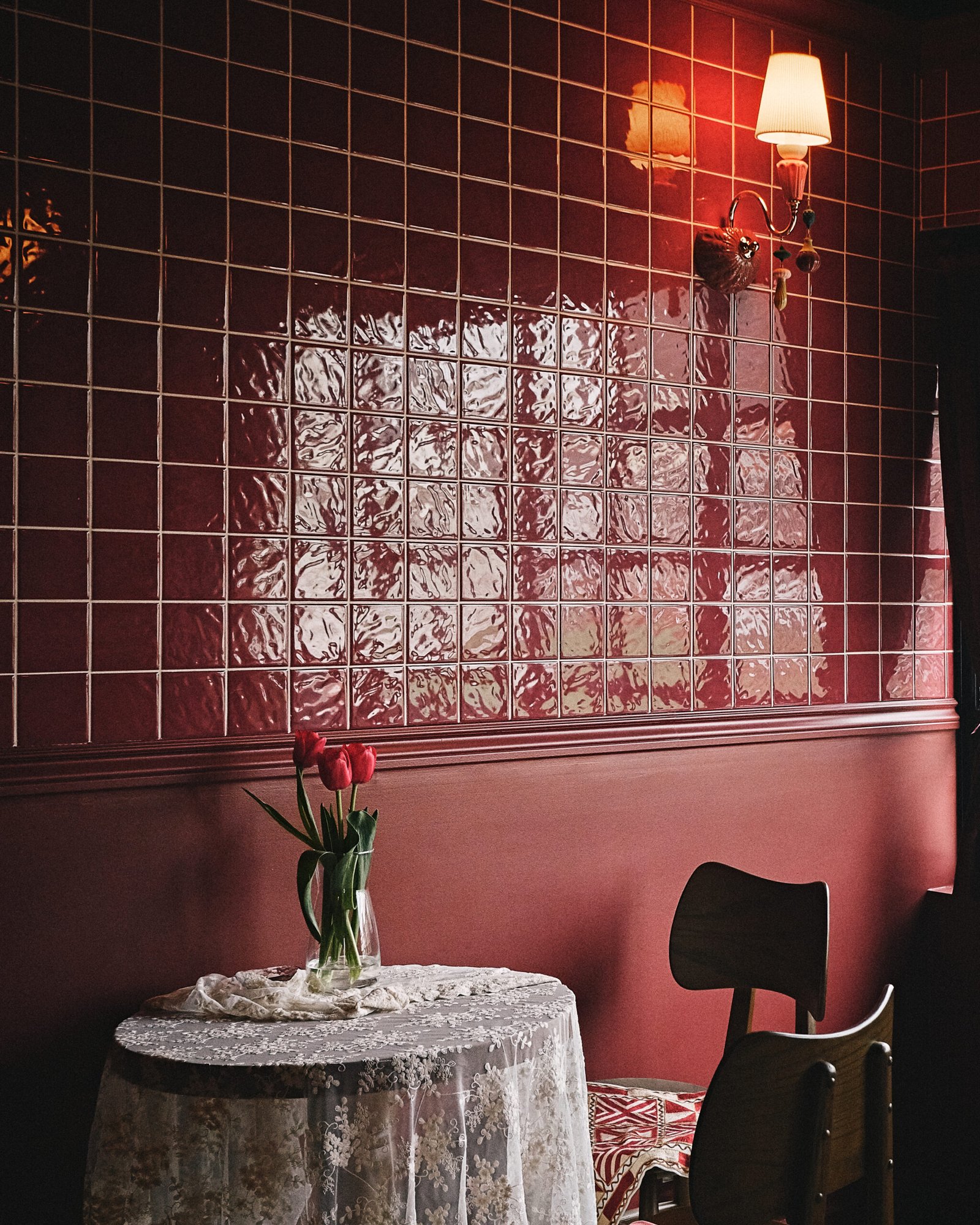 A vertical shot of a red cafe interior with tiled walls, a small table and two wooden chairs.