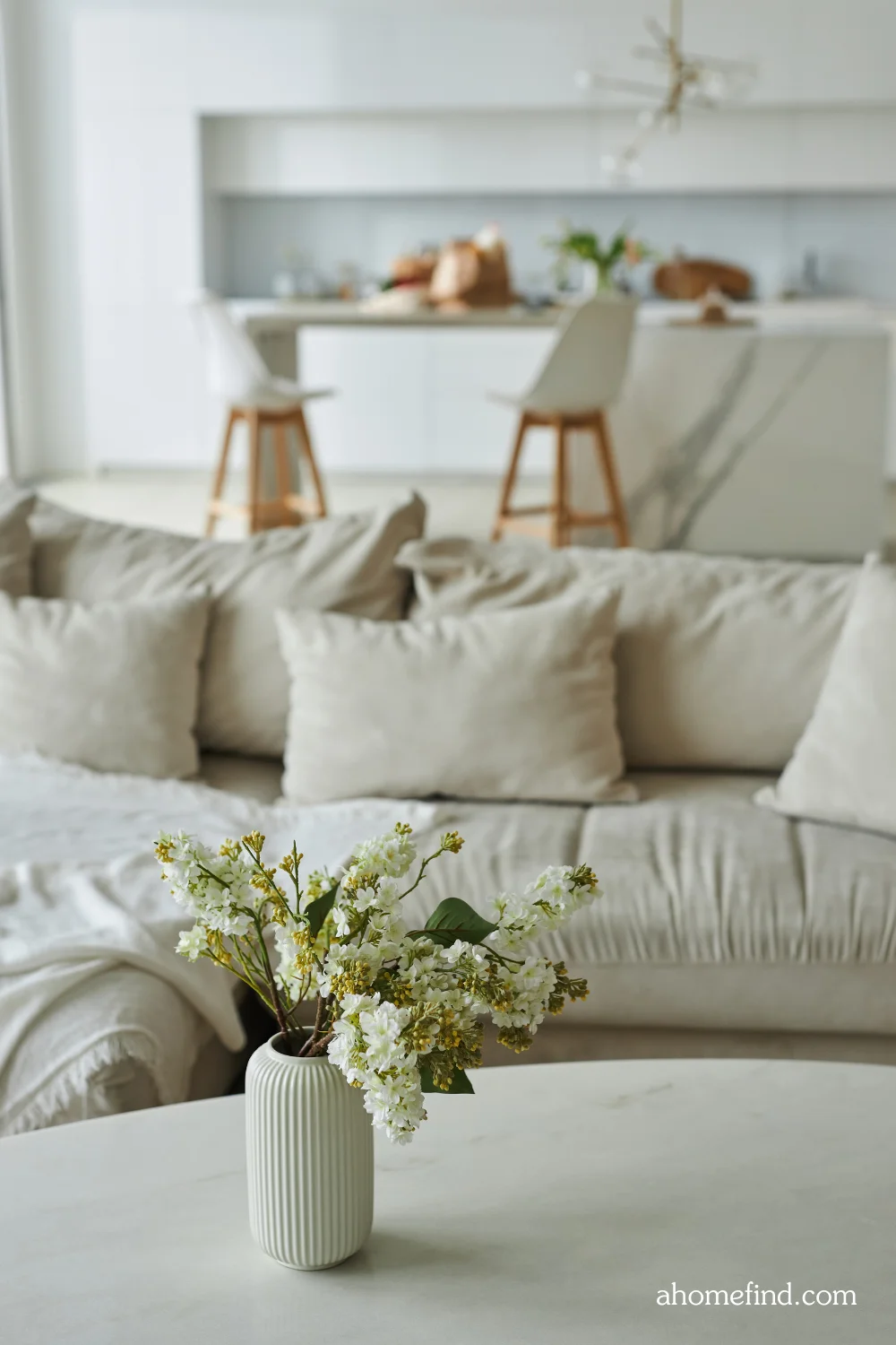 cheap and chic apartment decor in neutral colors. A beige sofa and a coffee table with a flower on it. In the background is a kitchen. Scaled. 