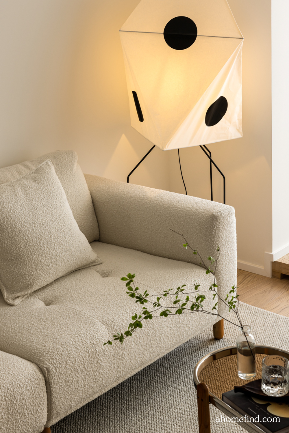 A beige couch and a floor lamp. A wooden coffee table with a flower on it. Scaled. 