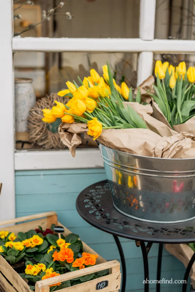 Spring front porch decor with yellow tupils on a side table and a box with Floral front porch arrangements.