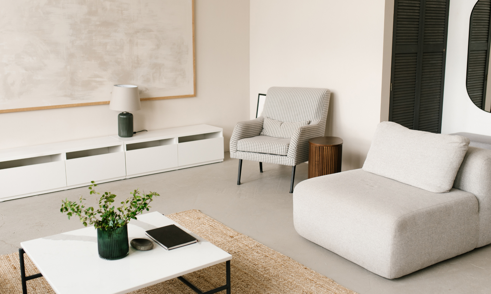 A minimalist living room with two armchairs, a coffee table, a large wall art and decor pieces.