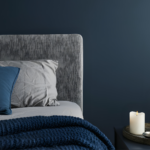 A moody dark blue bedroom with bedside table and dark blue bedding.