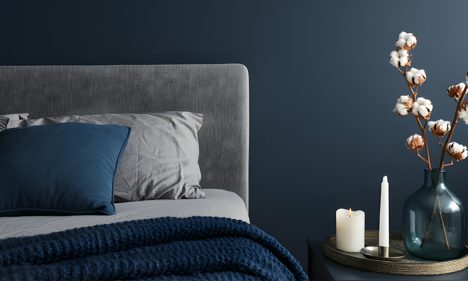 A moody dark blue bedroom with bedside table and dark blue bedding.