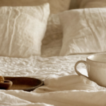 Closeup on perfect bed sheets in a white color, a wooden brick and a coffee mug. Scaled.