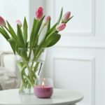 Spring tulips on a side table and a burning candle. In the background is a sofa. Scaled. Spring Home Decor.