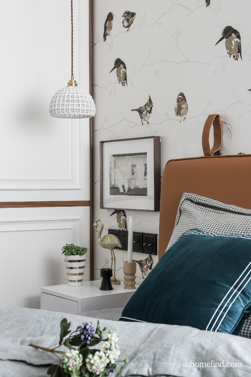 Small bedroom design with a wallpaper with birds, teal pillows and a brown bed frame. Decorative details. 