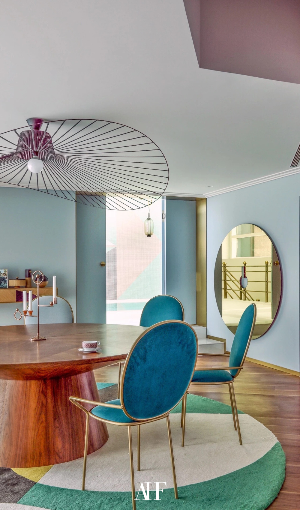 Curved edges with a round rug and a round wooden dining table with teal chairs with rounded edges.