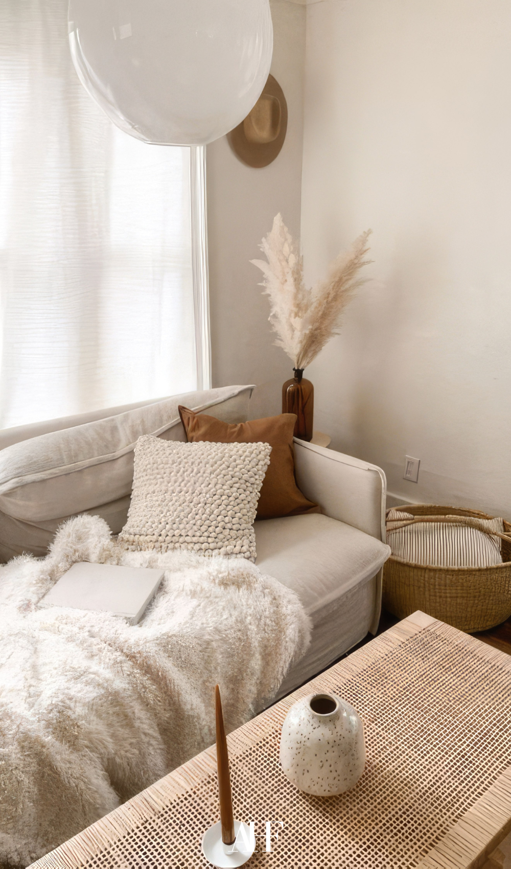 A cozy, light-filled corner featuring a white sofa, sandy beige and rust throw pillows, sheer linen curtains. Summer Interior Design Trends.