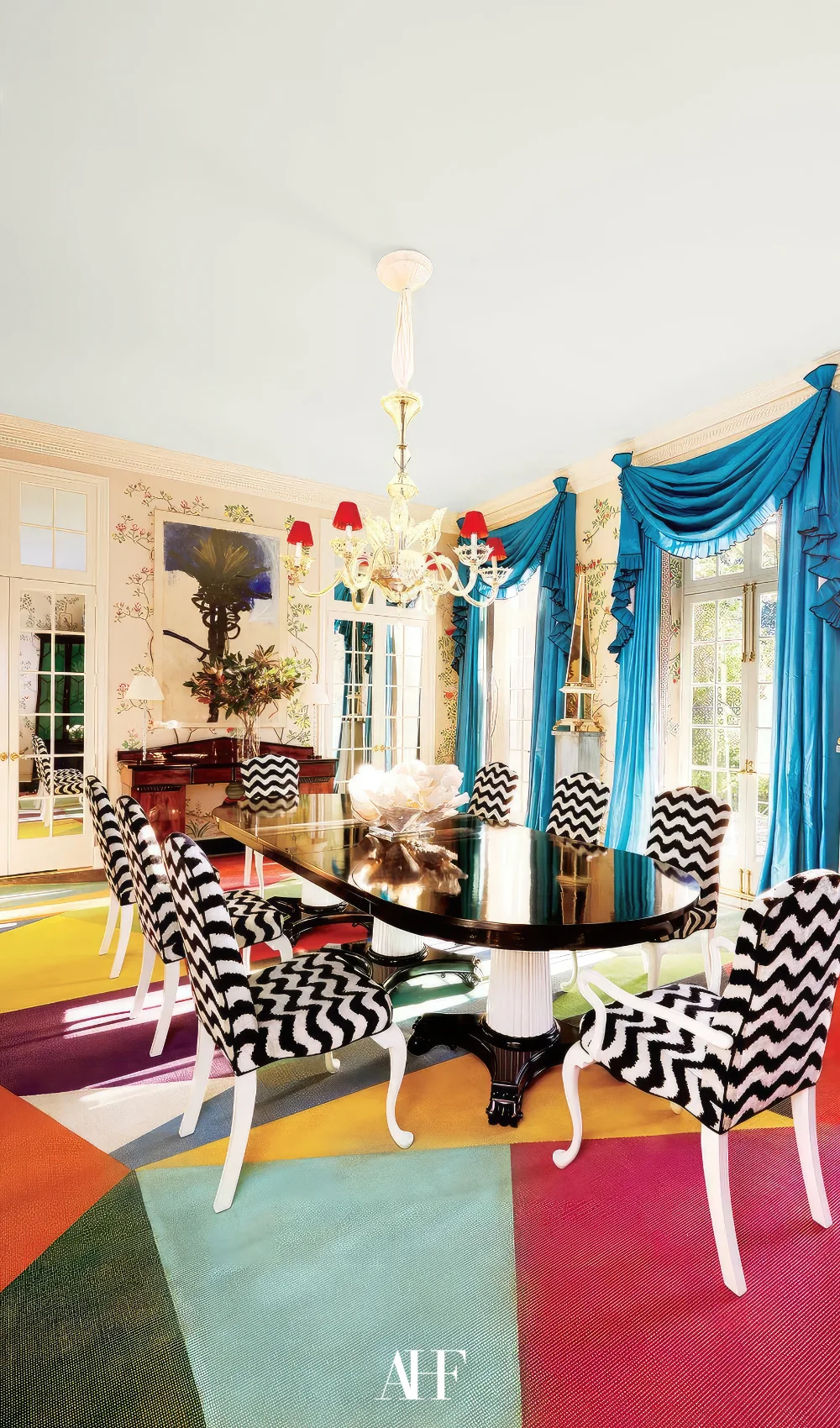A bold interior design with a colorful rug, black and white chairs and blue curtains in the windows.