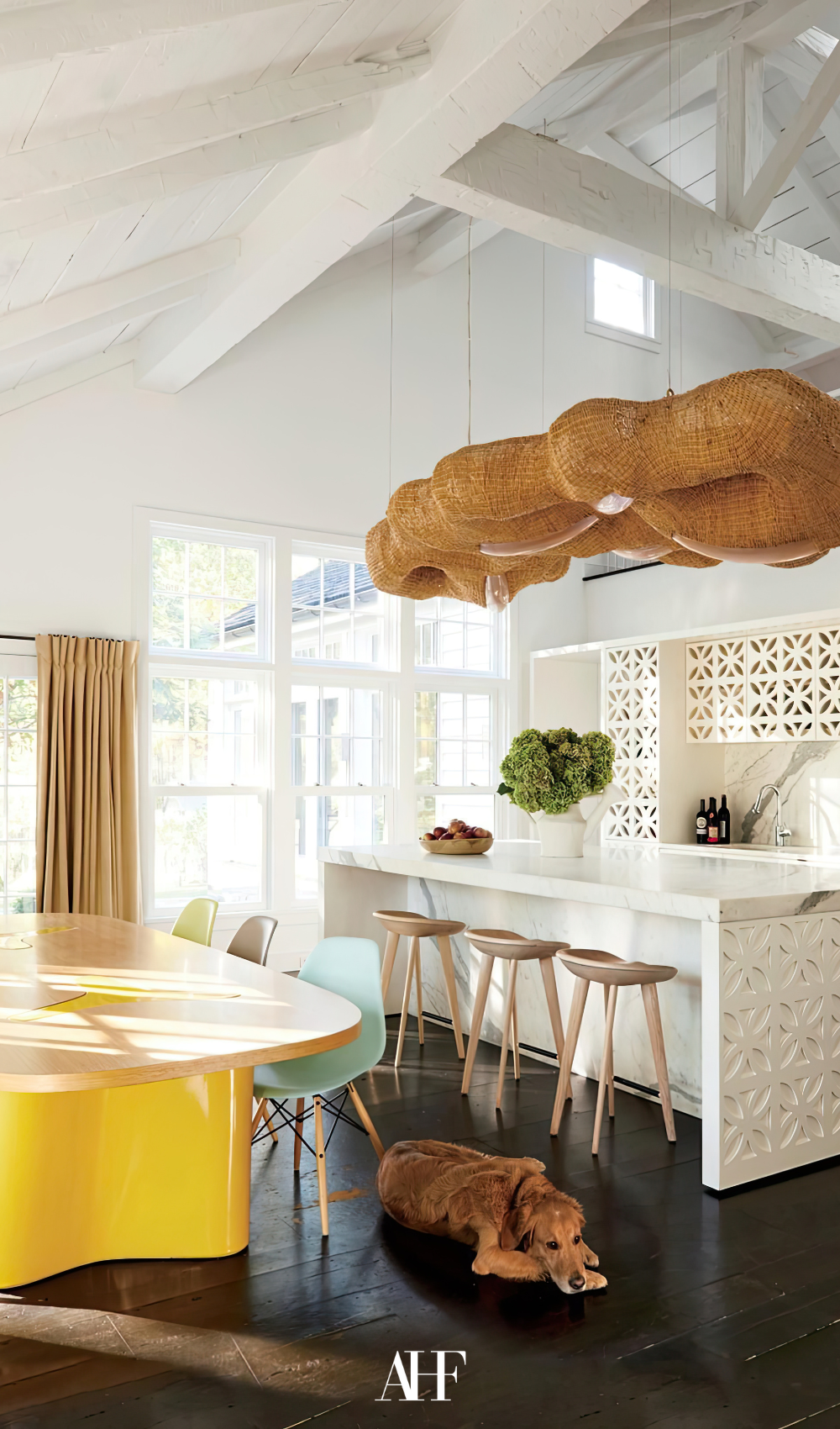 A light summer kitchen with a large yellow kitchen table, a kitchen island and large ceiling lamps.