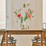 A summer wooden dining table with wooden dining chairs. A floral centerpiece.