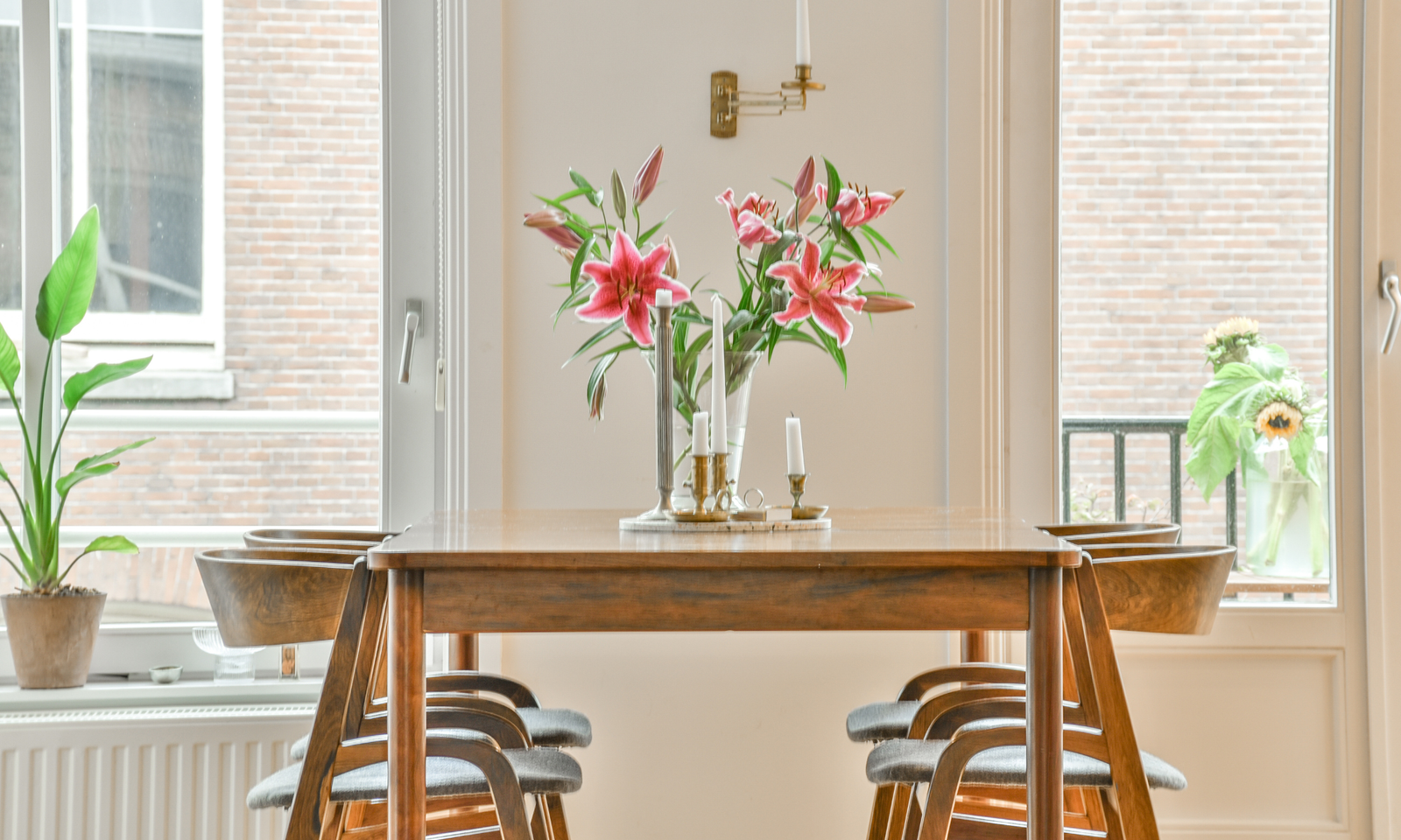 A summer wooden dining table with wooden dining chairs. A floral centerpiece.