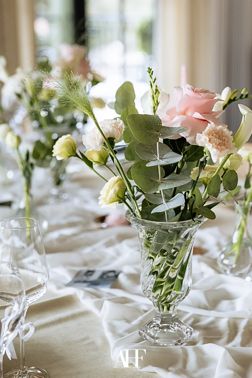 Elegant dining setup with a glass vase with flowers and linen table cloth.